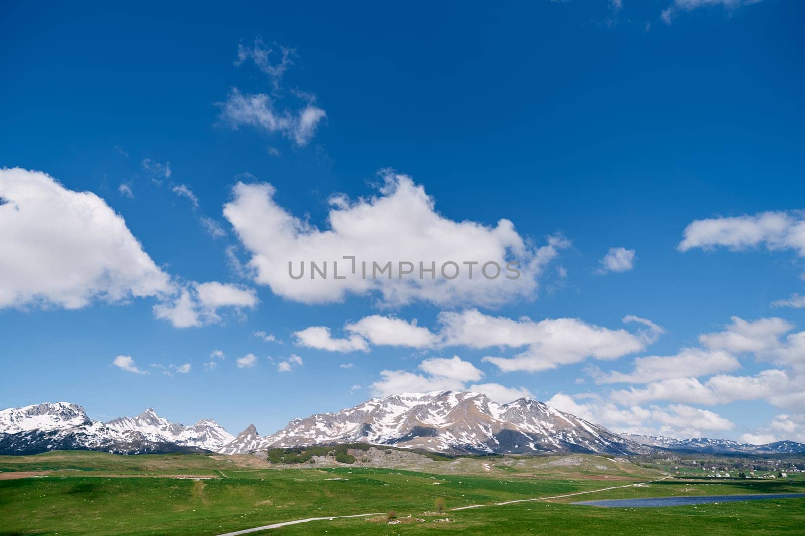 Green valley with a lake against the backdrop of snowy mountains. Durmitor, Montenegro by Nadtochiy