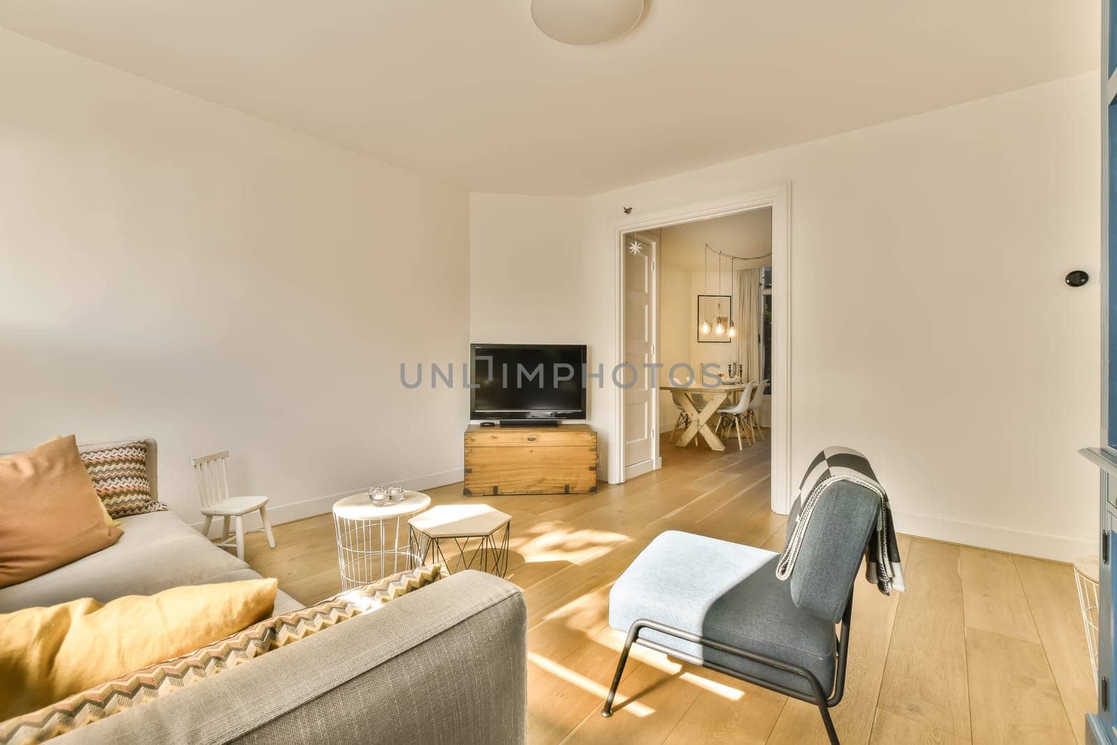 a living room with white walls and hardwood flooring, including a grey sofa set in the center of the room