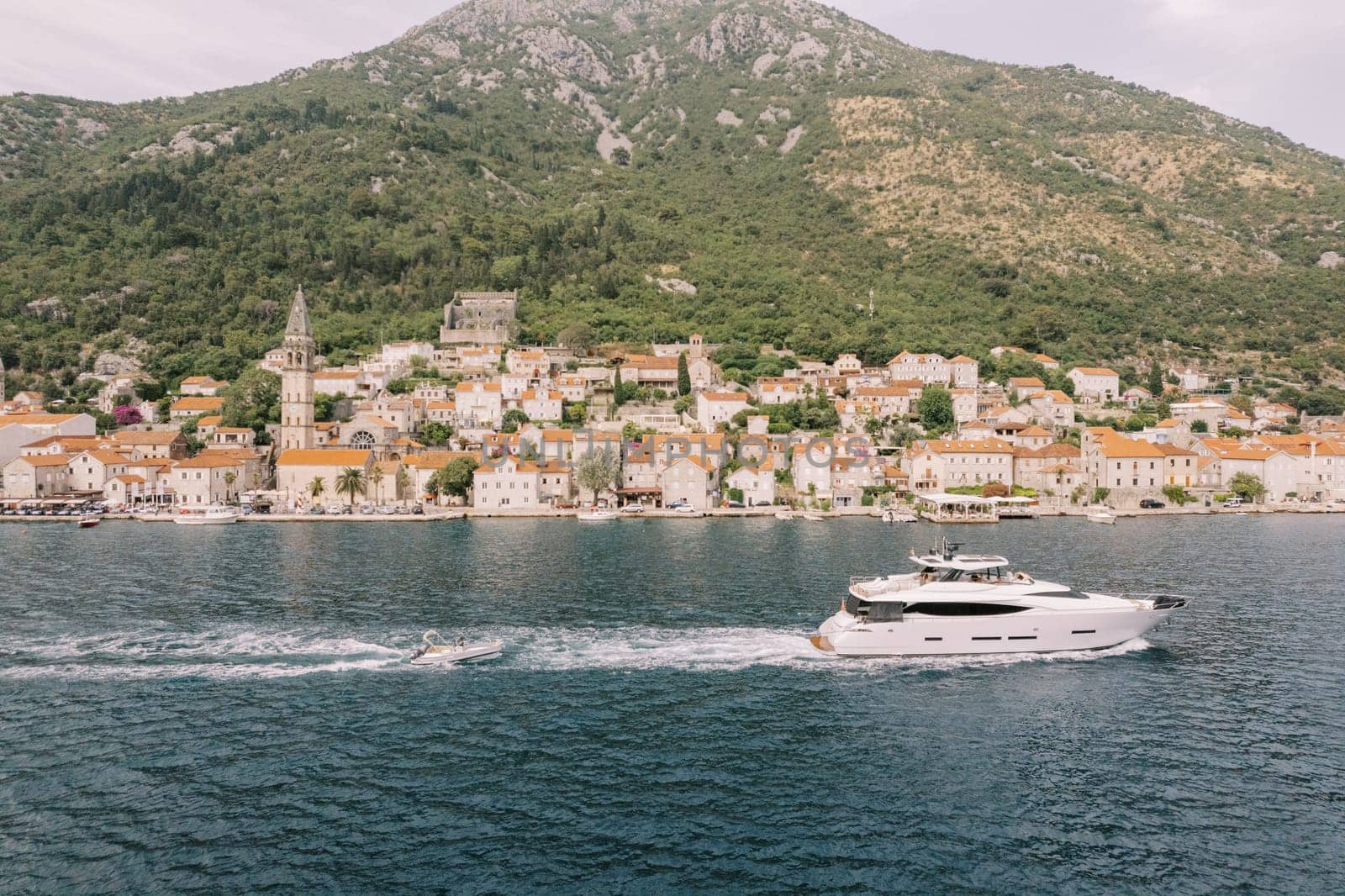 Motor yacht sails the sea along the coast of an ancient town. Perast, Montenegro. Drone by Nadtochiy