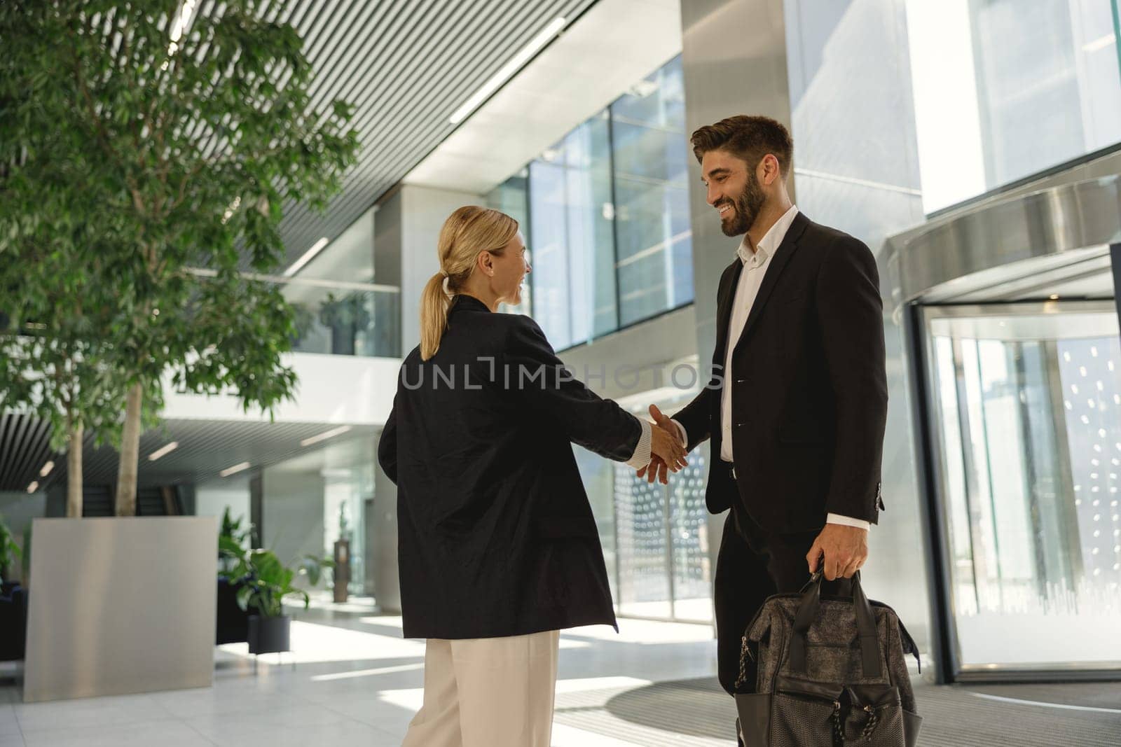 Business partners in suits shaking hands in front of the modern office background by Yaroslav_astakhov