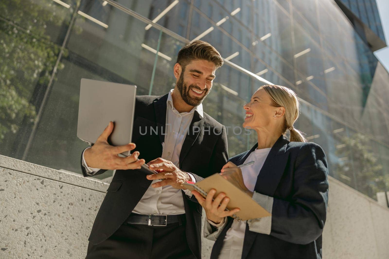 Business colleagues working on project while sitting outdoors on skyscrapers background