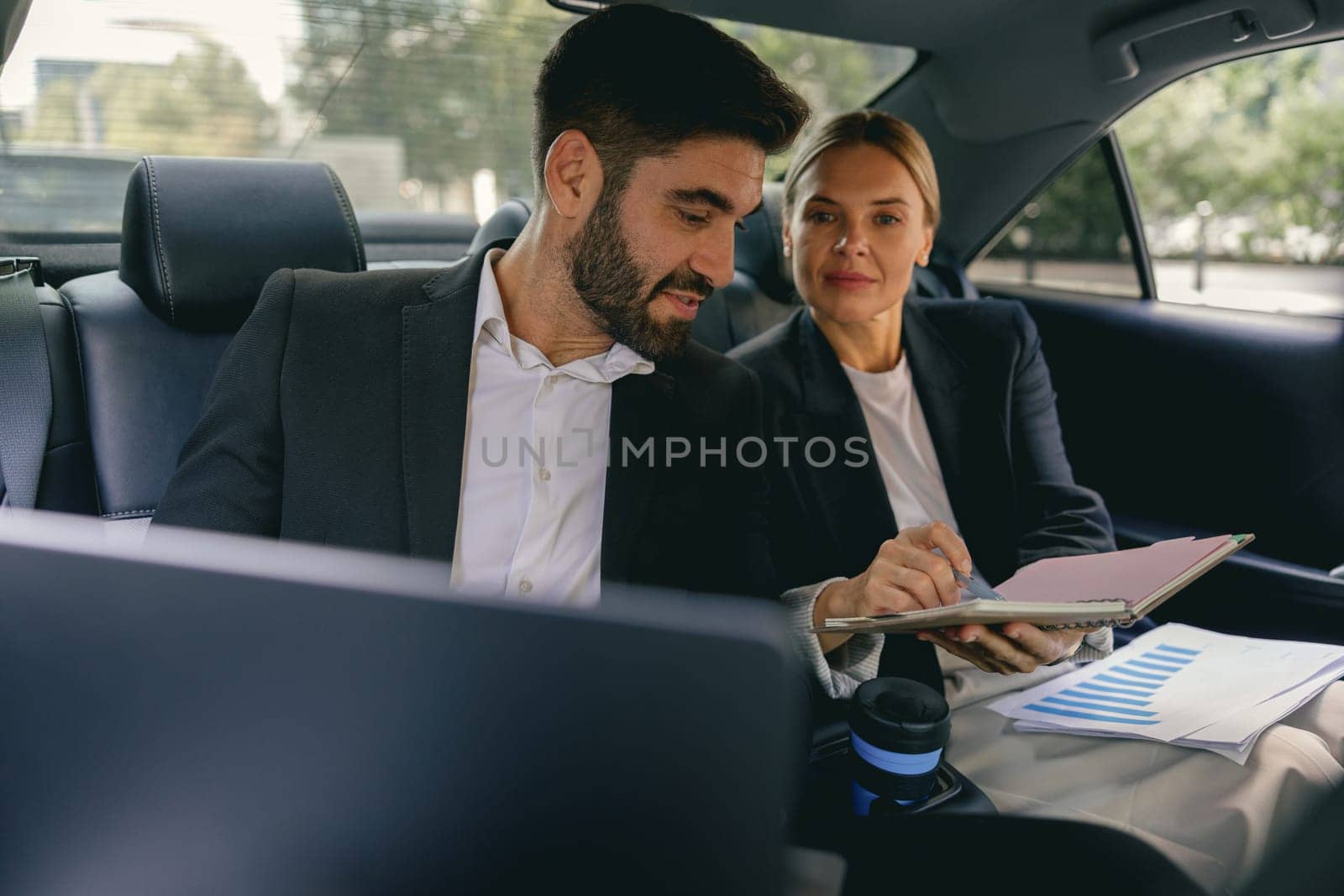 Cheerful business people have online meeting using laptop while sitting in car back seats