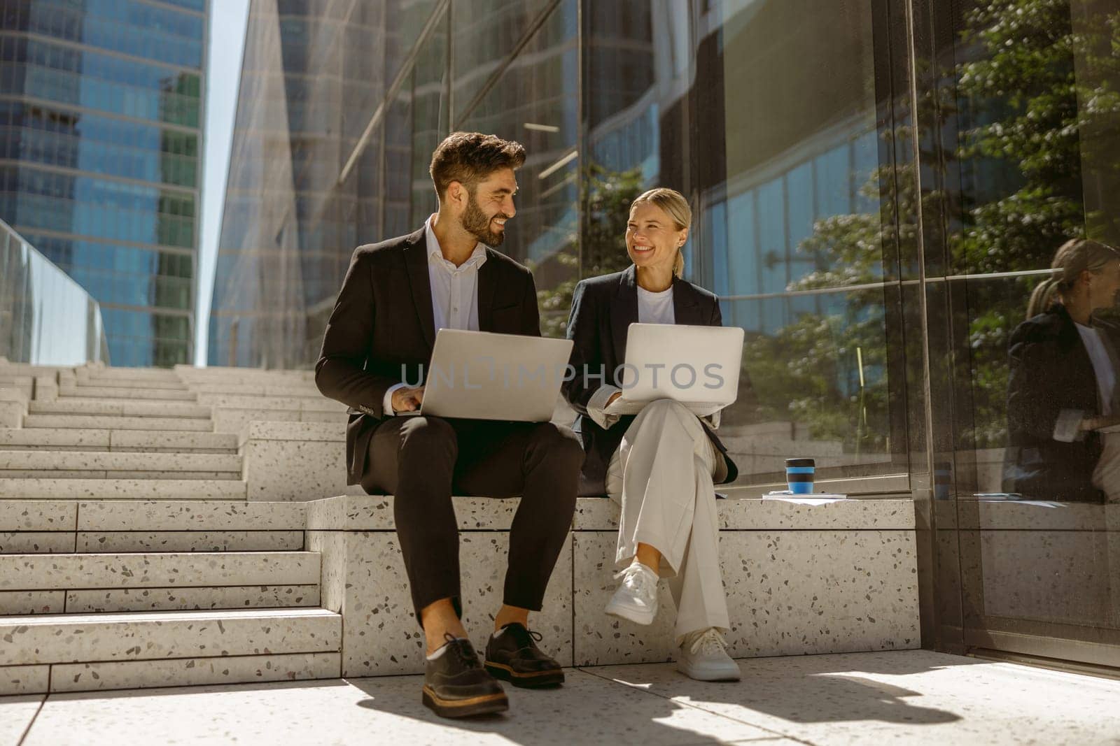 Man and woman in classic suit discussing business details and using laptop while sitting outdoors by Yaroslav_astakhov