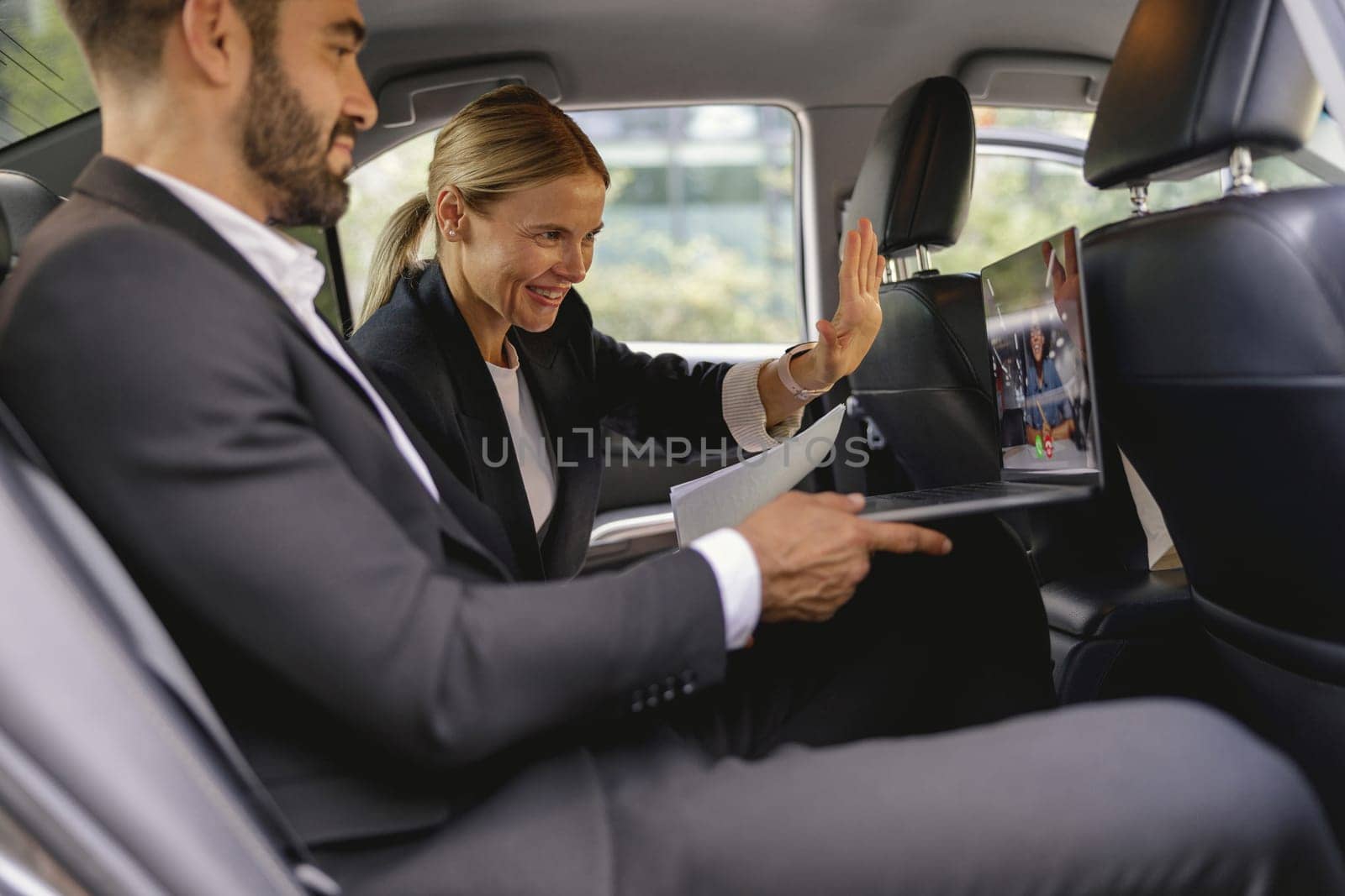 Cheerful business people have online meeting using laptop while sitting in car back seats by Yaroslav_astakhov