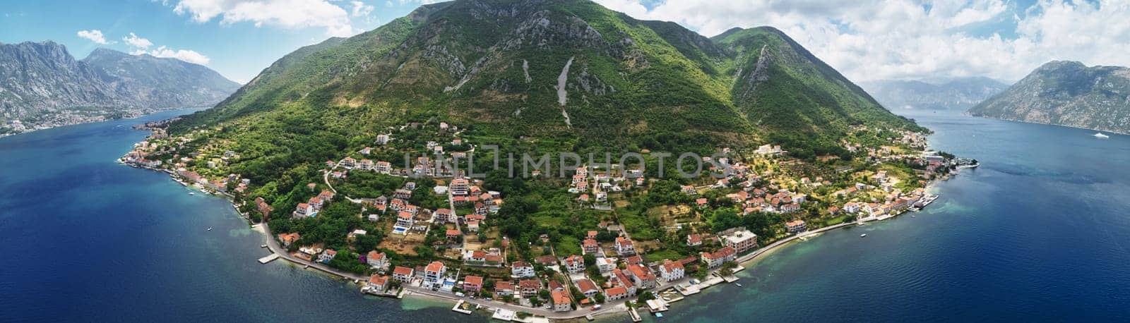 Old houses with red roofs on the seashore on the slope of a green mountain. Montenegro. Drone. Panorama by Nadtochiy