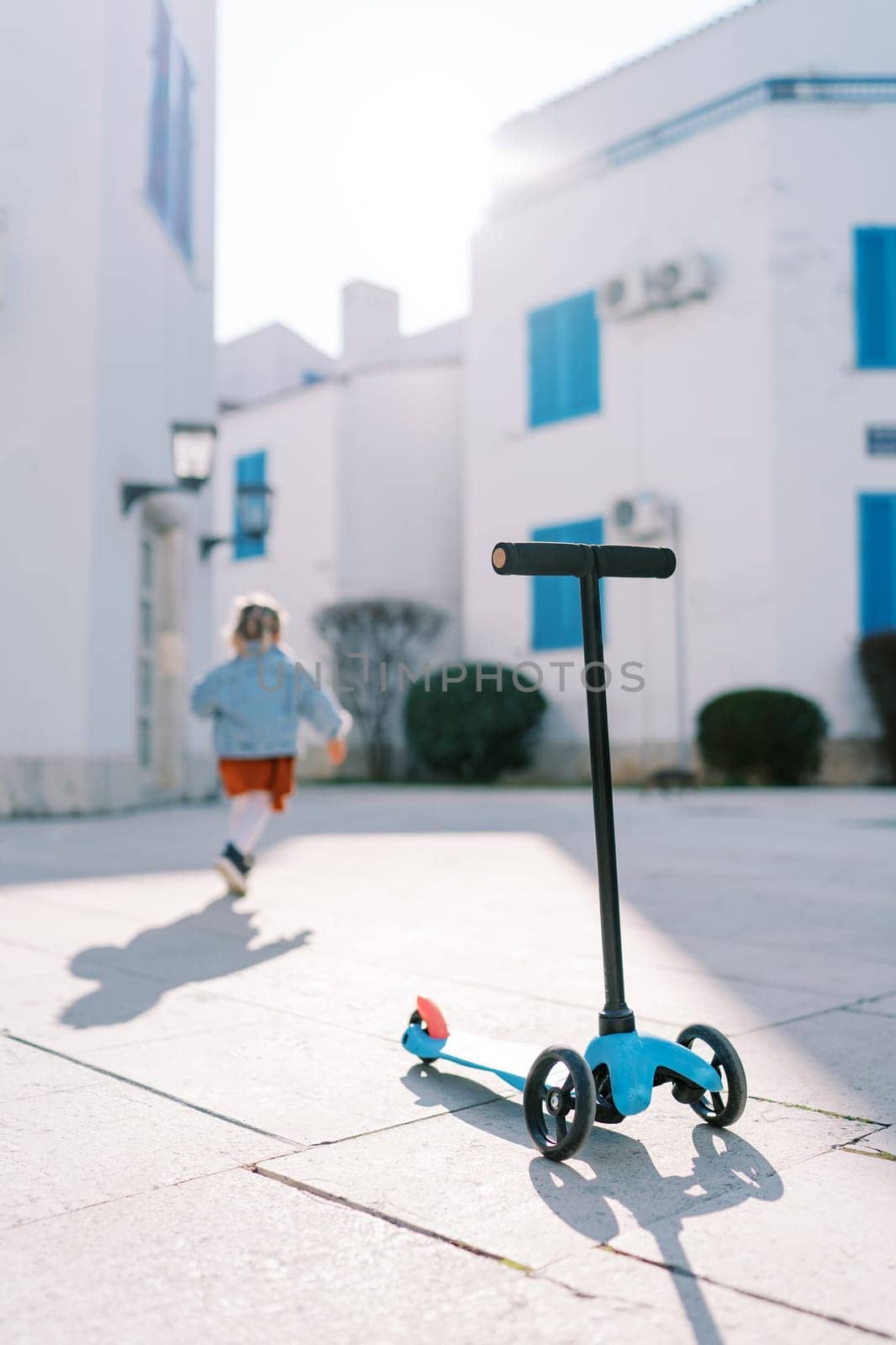 Scooter stands on a tile in the courtyard of the house against the background of a little girl walking forward. High quality photo