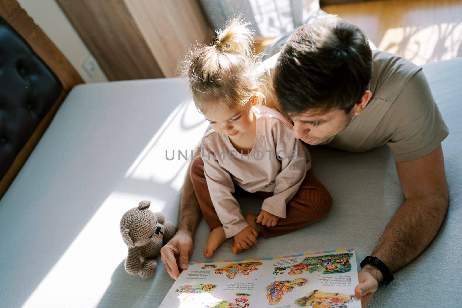 Smiling little girl listening to dad reading a fairy tale on the bed. High quality photo
