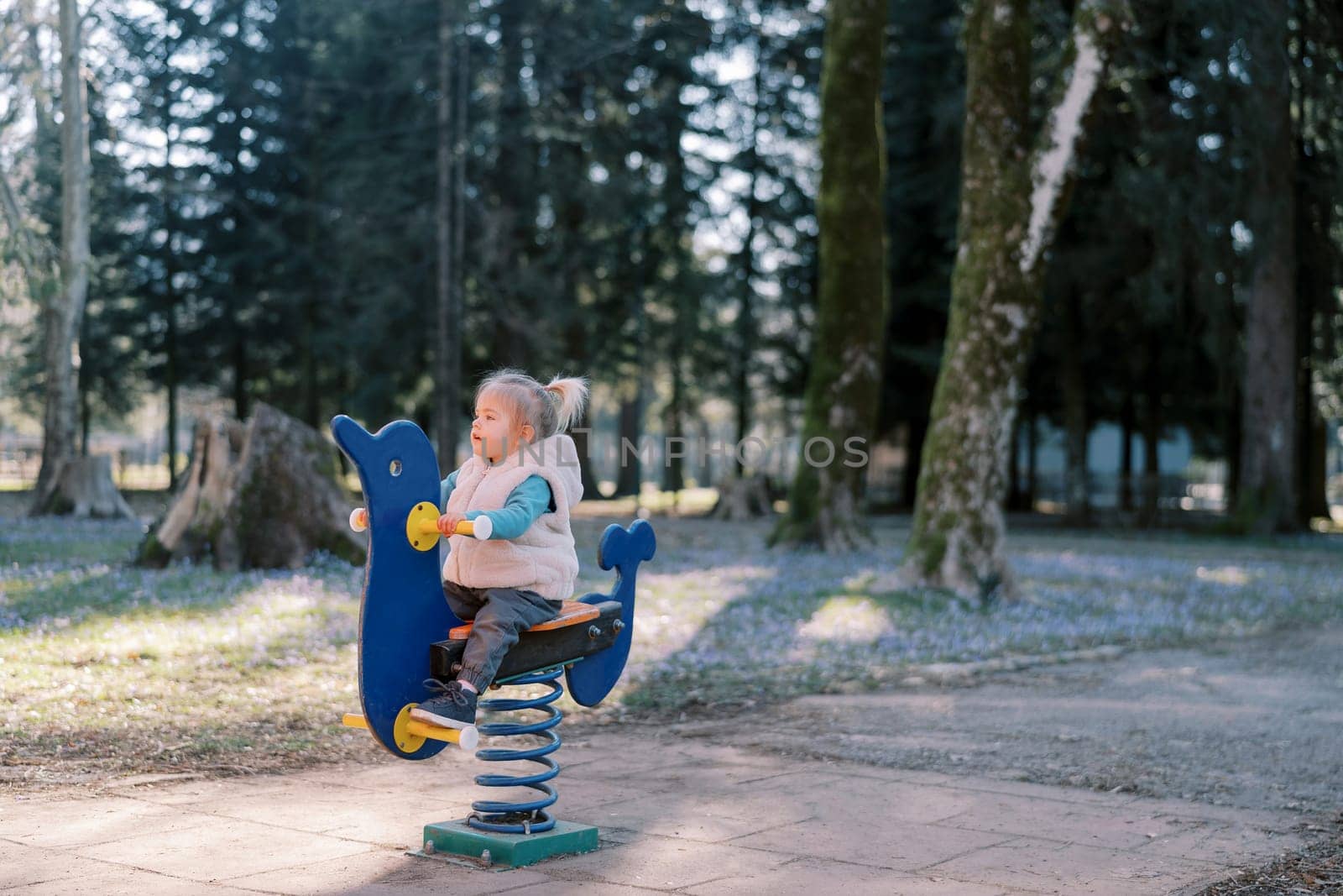 Little girl sitting on a swing-spring holding the handles on the playground. High quality photo