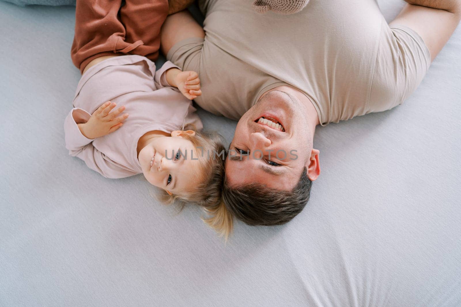 Smiling dad with little daughter lie on the bed, touching the tops. Top view. High quality photo