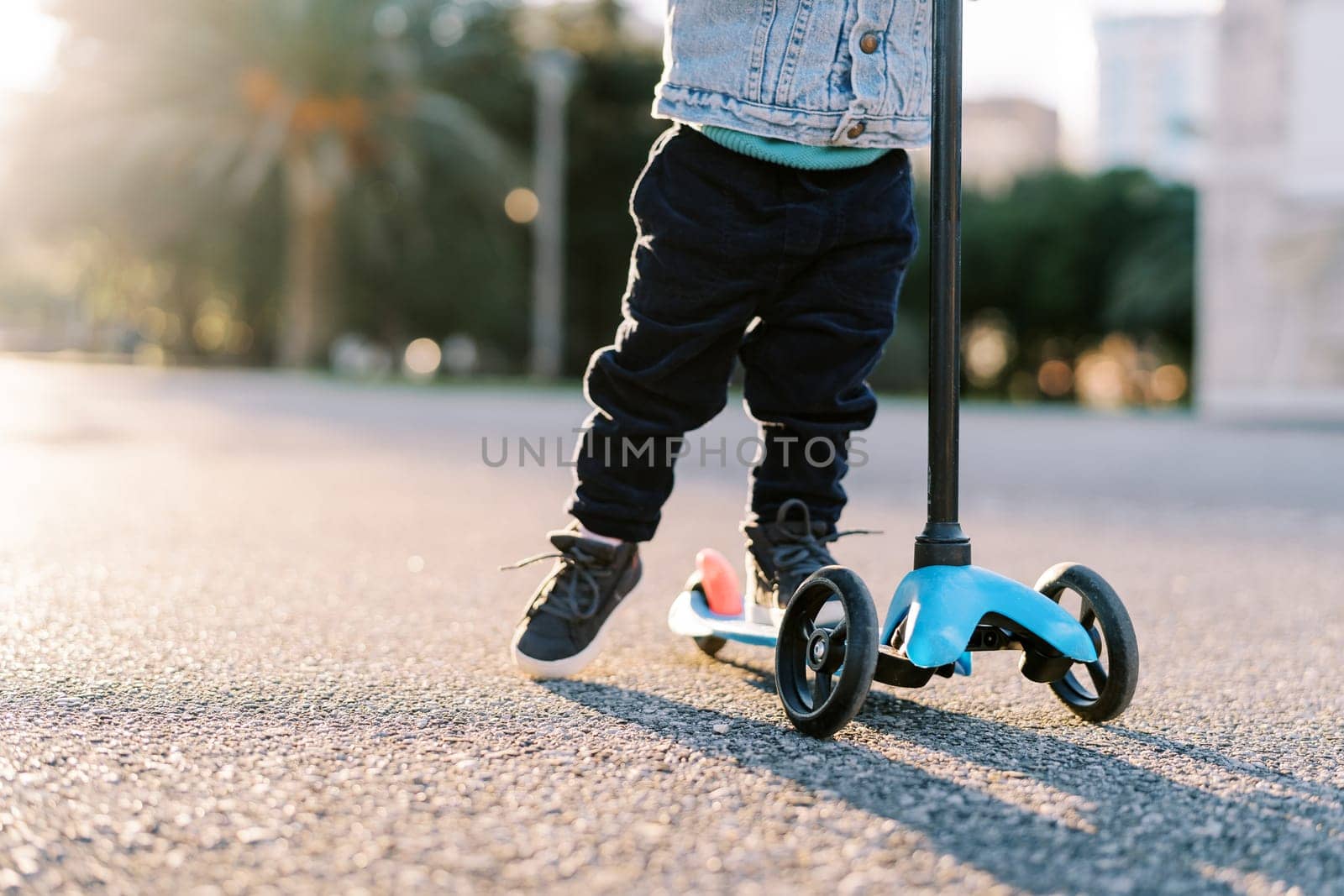 Small child rides a scooter along the road, pushing off with his foot. Cropped. Faceless. High quality photo