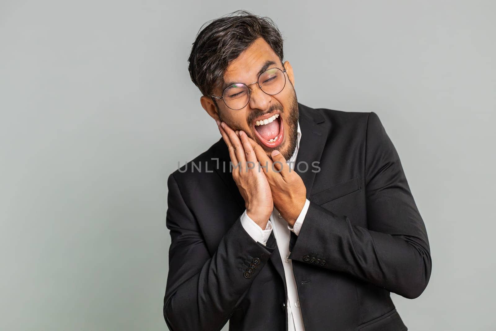 Dental problems. Indian businessman touching cheek, closing eyes with expression of terrible suffer from painful toothache, sensitive teeth, cavities. Male Arabian man guy isolated on gray background