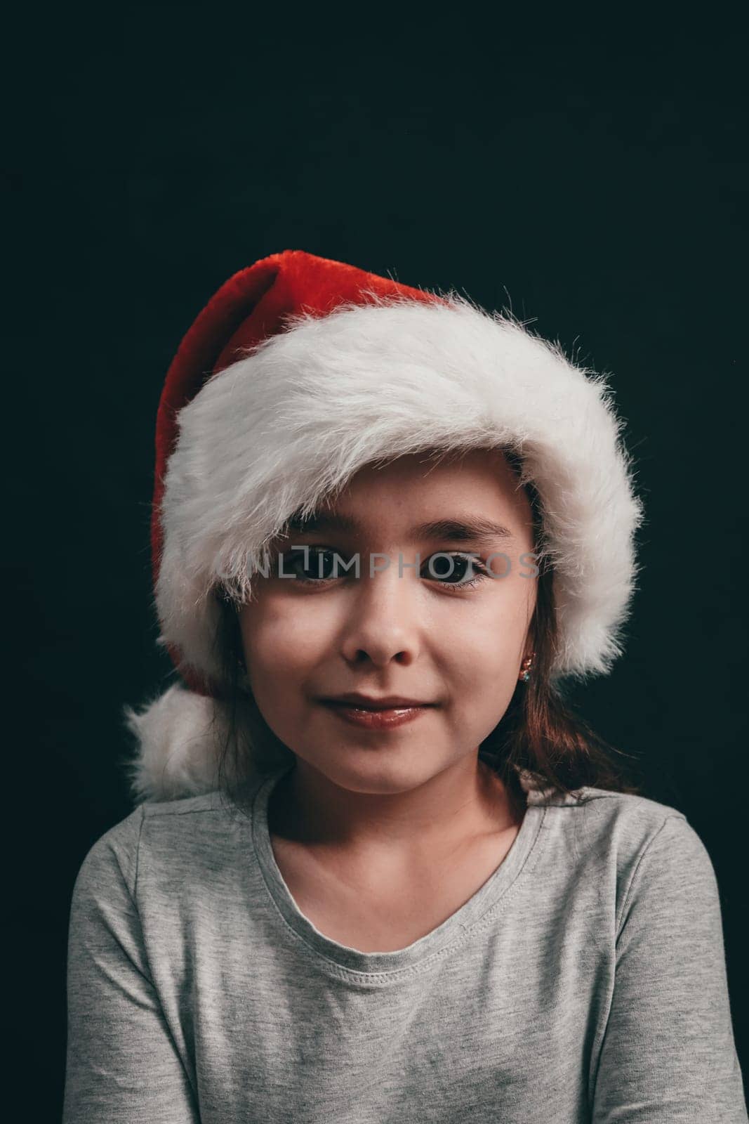 Portrait of a little caucasian girl in a santa claus hat with a cheerful emotion on a black background, close-up side view.
