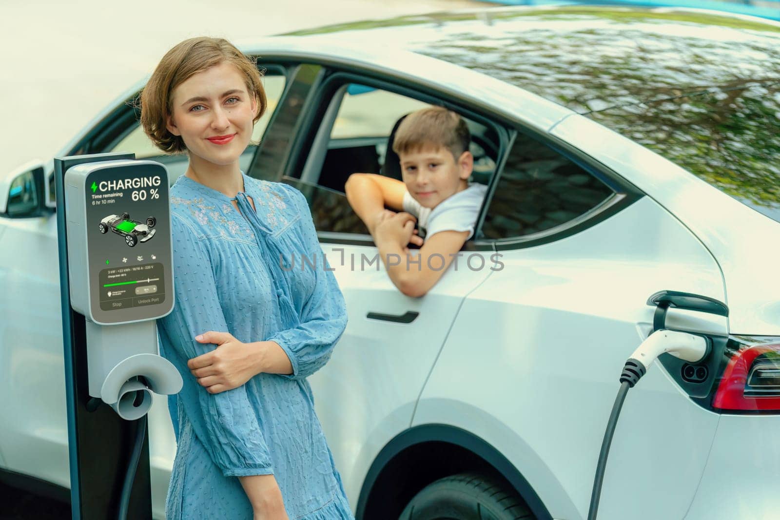 Environmental awareness family with eco-friendly electric car recharging battery from home EV charging station with little boy inside the car. Rechargeable and EV car technology. Perpetual