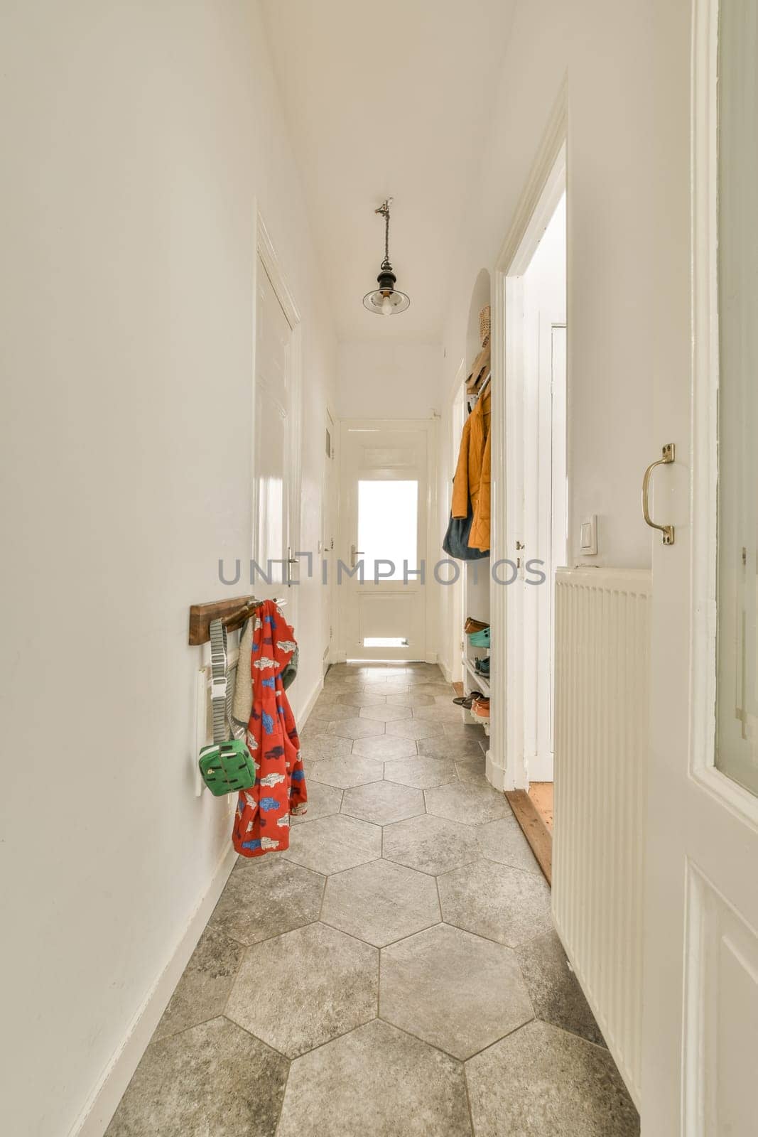 a long hallway with white walls and grey tiles on the floor, there is an open door leading to another room