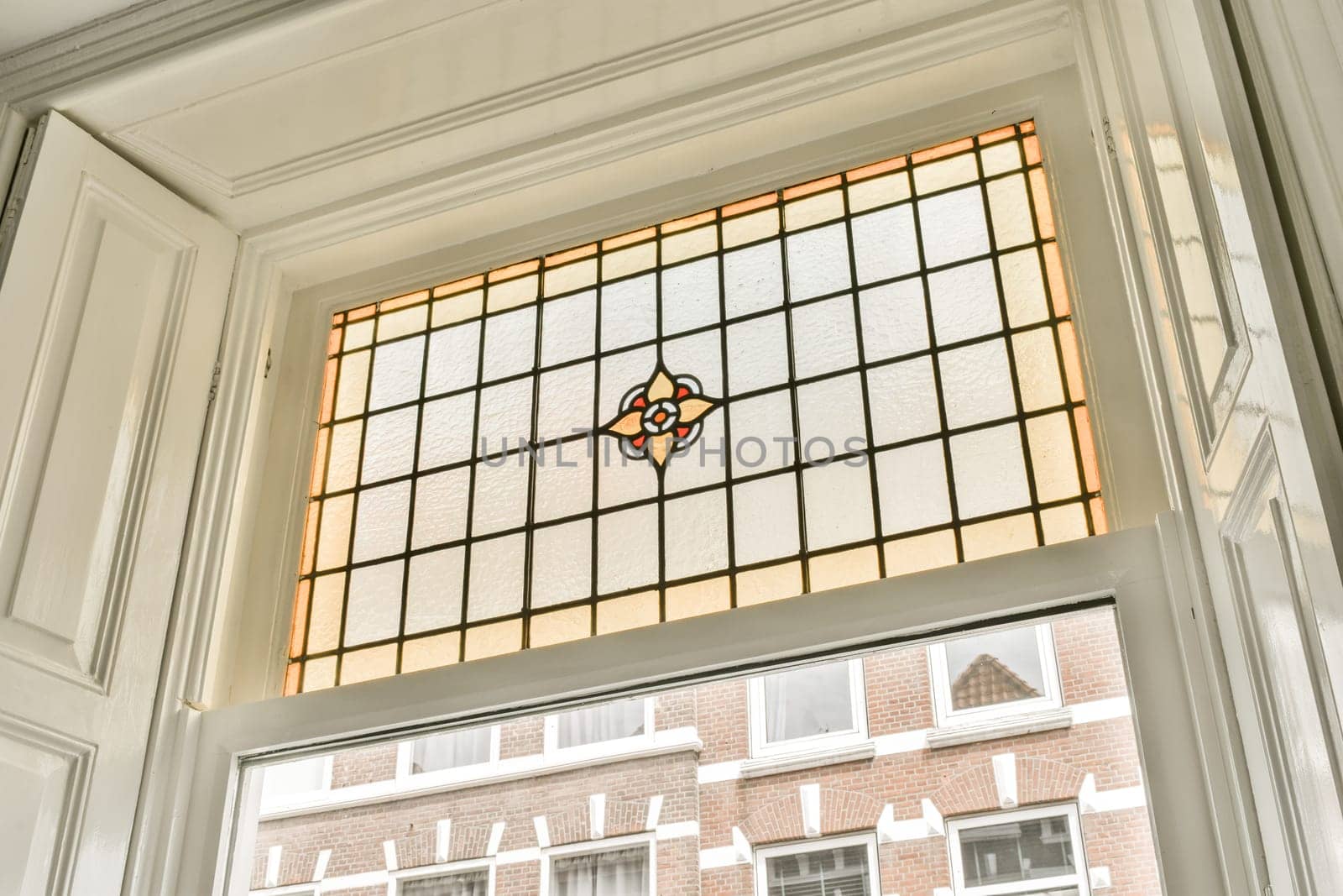 a stained glass window in a house with white trim on the windowsills, and a brick wall behind it