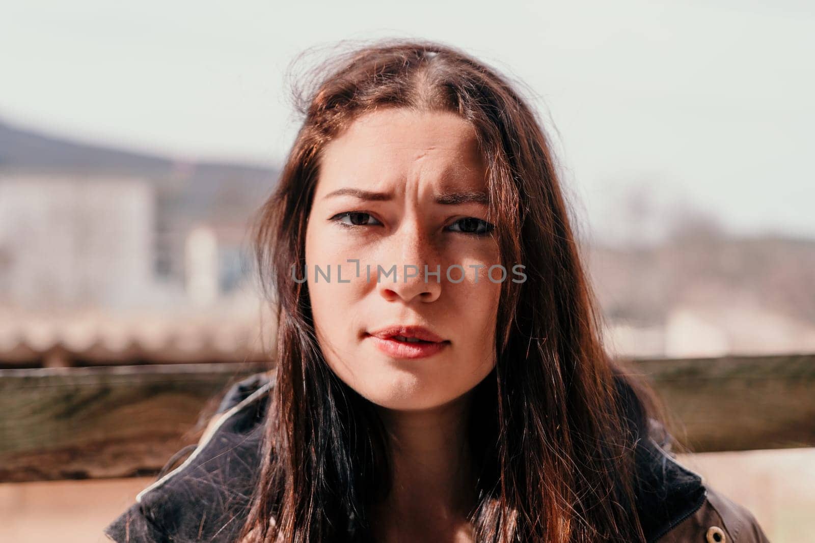 Happy young smiling woman with freckles outdoors portrait. Soft sunny colors. Outdoor close-up portrait of a young brunette woman and looking to the camera, posing against nature background.