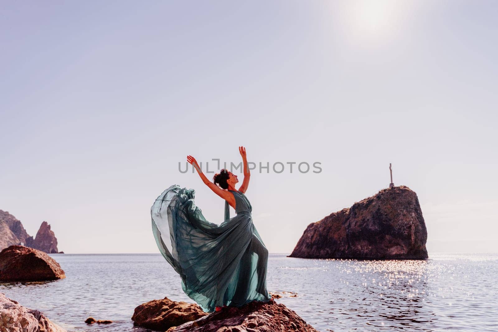 Woman green dress sea. Woman in a long mint dress posing on a beach with rocks on sunny day. Girl on the nature on blue sky background