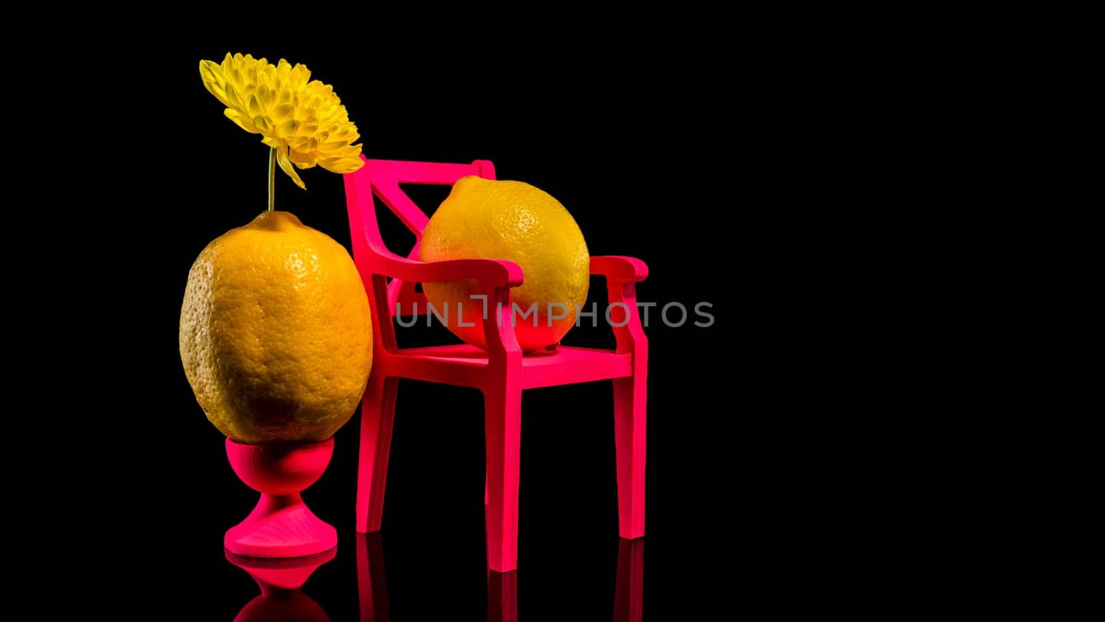 Creative still life with two lemons and pink chair on a black background