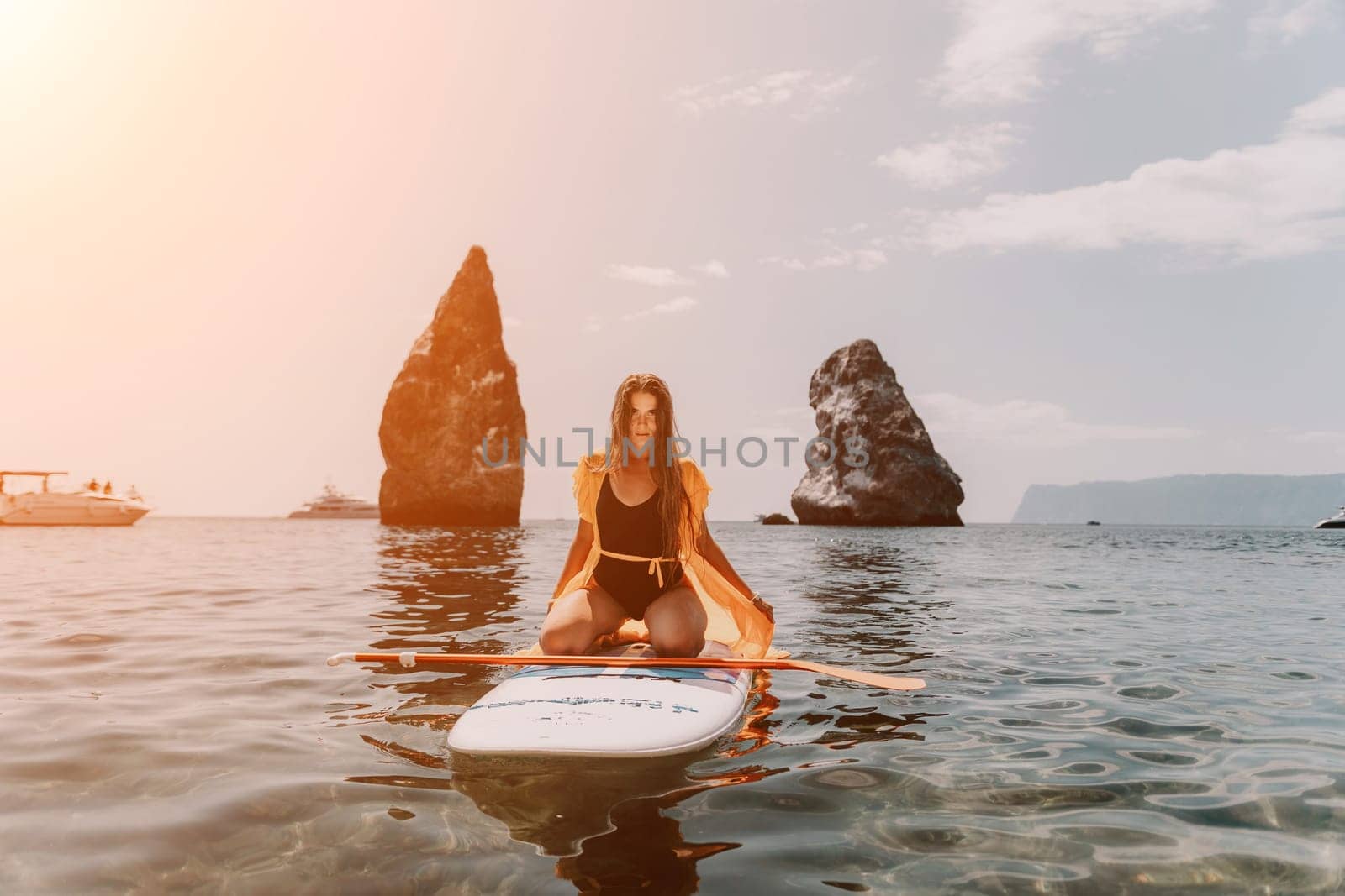 Close up shot of beautiful young caucasian woman with black hair and freckles looking at camera and smiling. Cute woman portrait in a pink bikini posing on a volcanic rock high above the sea