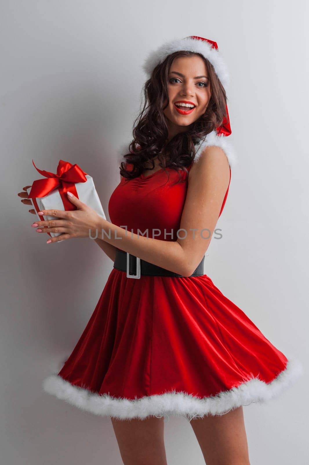 Beautiful young woman in Santa dress and hat celebrating Christmas holding gift box