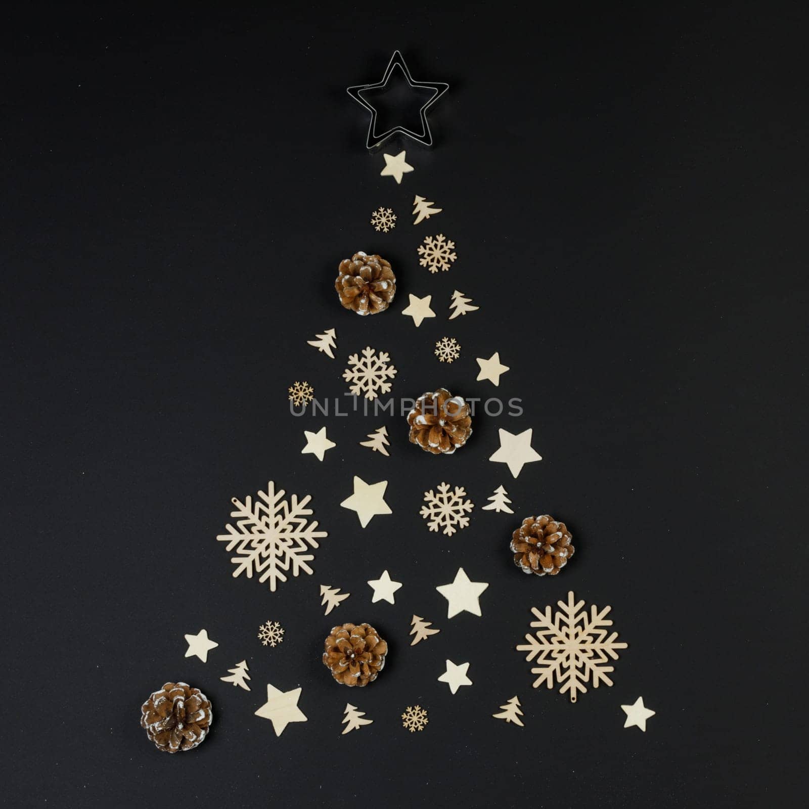 Christmas Tree made of wooden decor and pine cones on black paper background. Christmas Holiday Concept. Flat Lay