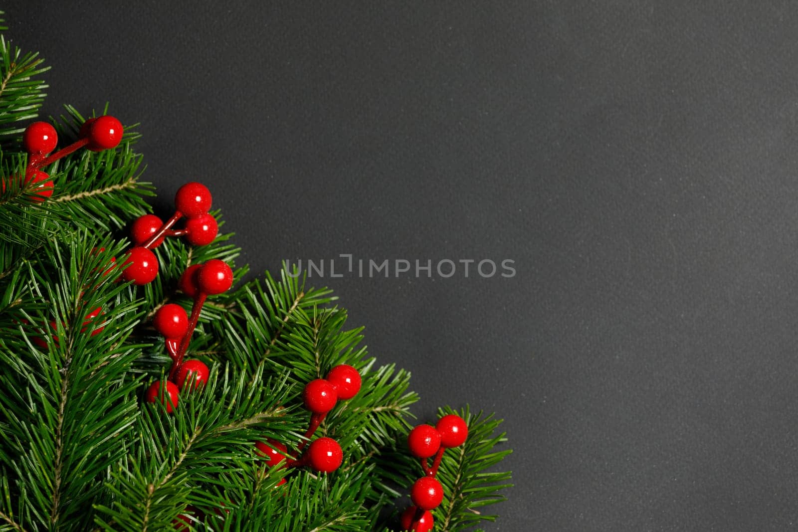 Pine Christmas tree branches and red berries on black paper background flat lay top view mock-up