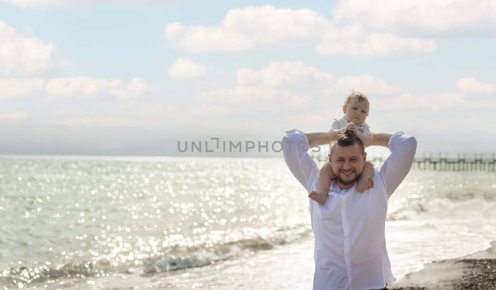 Happy father on vacation - smiling man holding his little baby son on his shoulders. Portrait