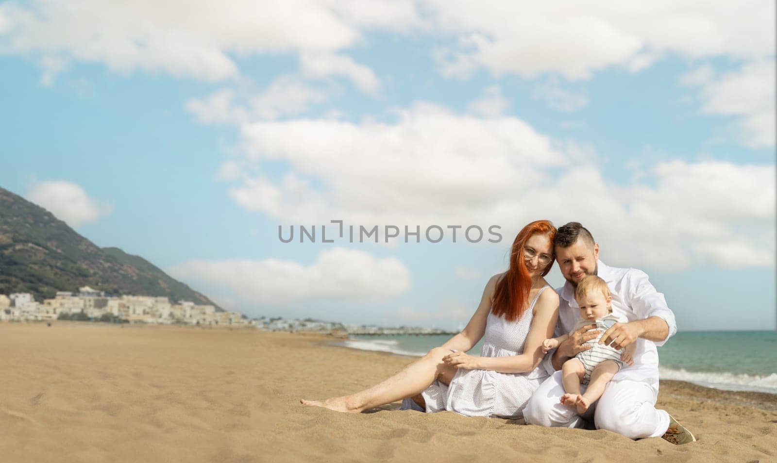 Happy family on vacation sitting on a sand beach with a baby son by Studia72