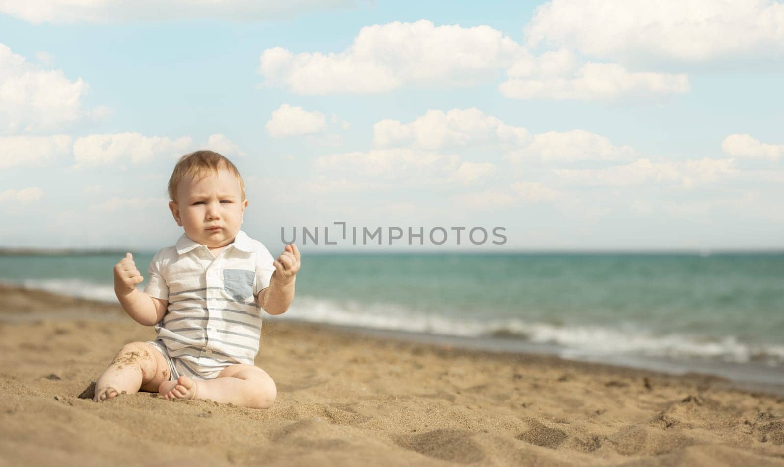 A baby boy sitting on a sand on the seaside. Mid shot