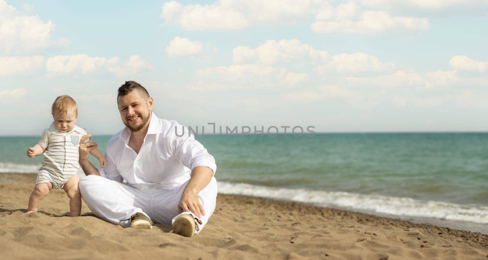 Happy father sitting on a beach with his little son by Studia72