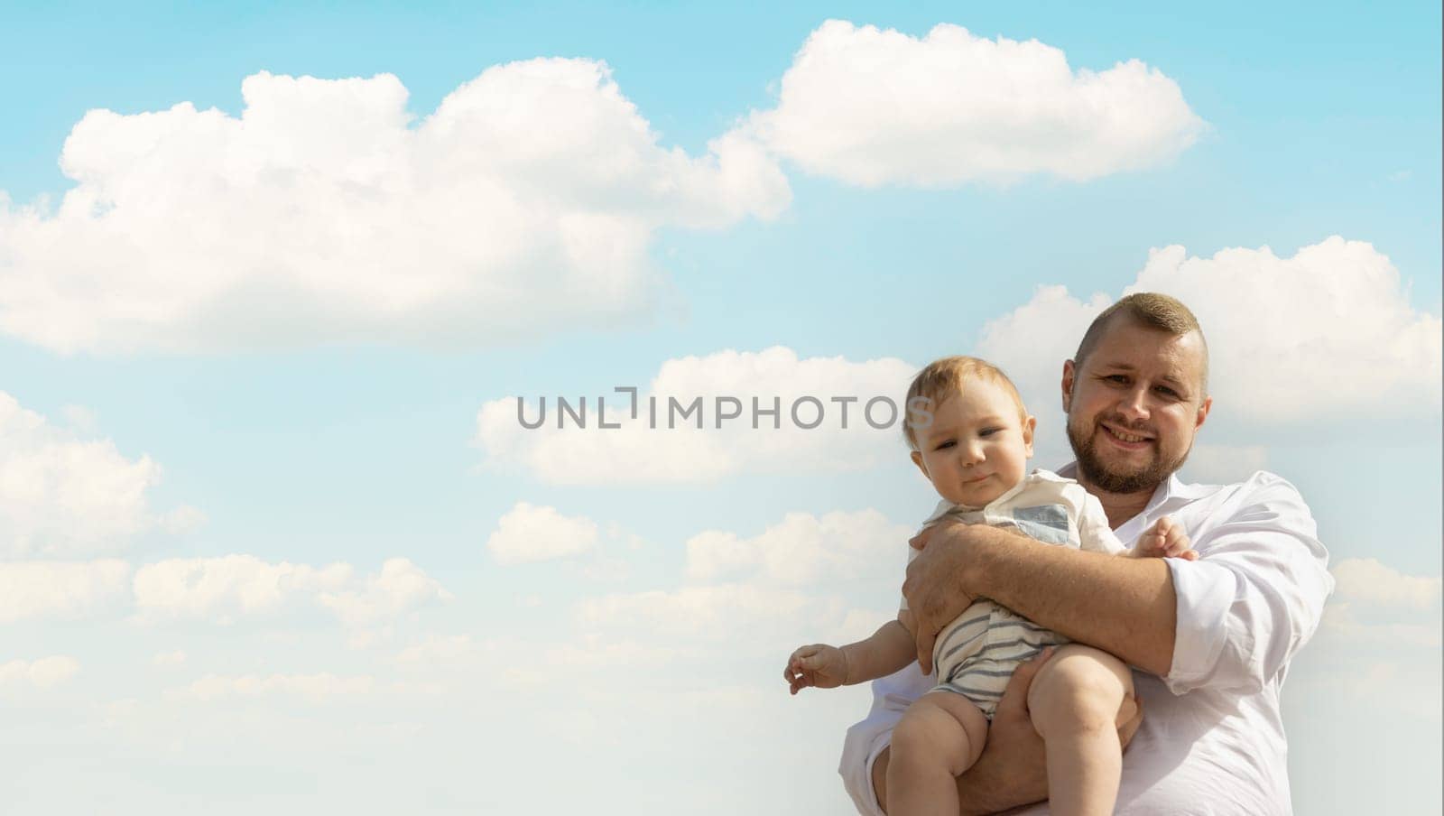Happy father on vacation - man holding his little baby son on sky background. Portrait