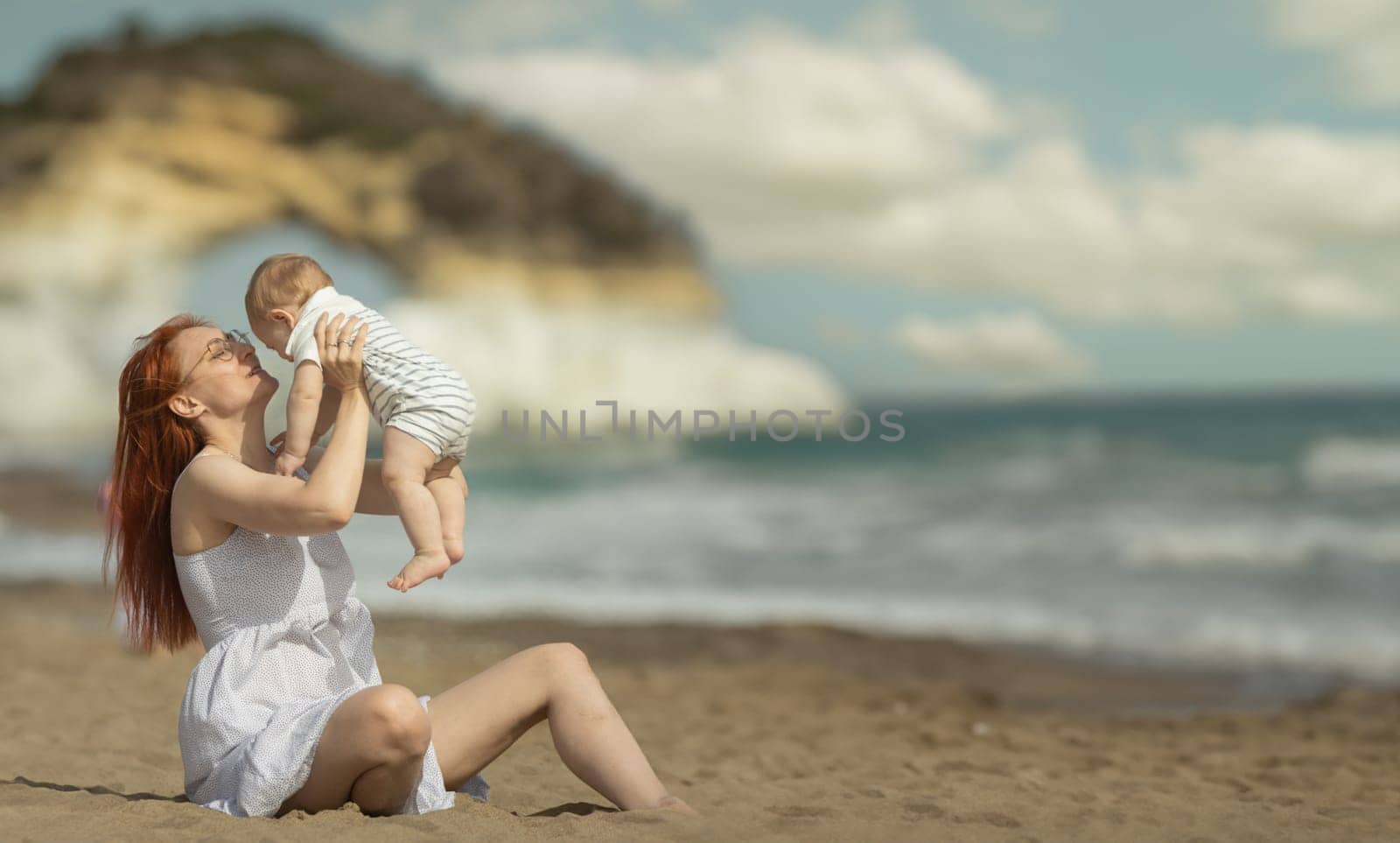 Happy mother and her little son resting on the seaside - raising the baby up. Mid shot
