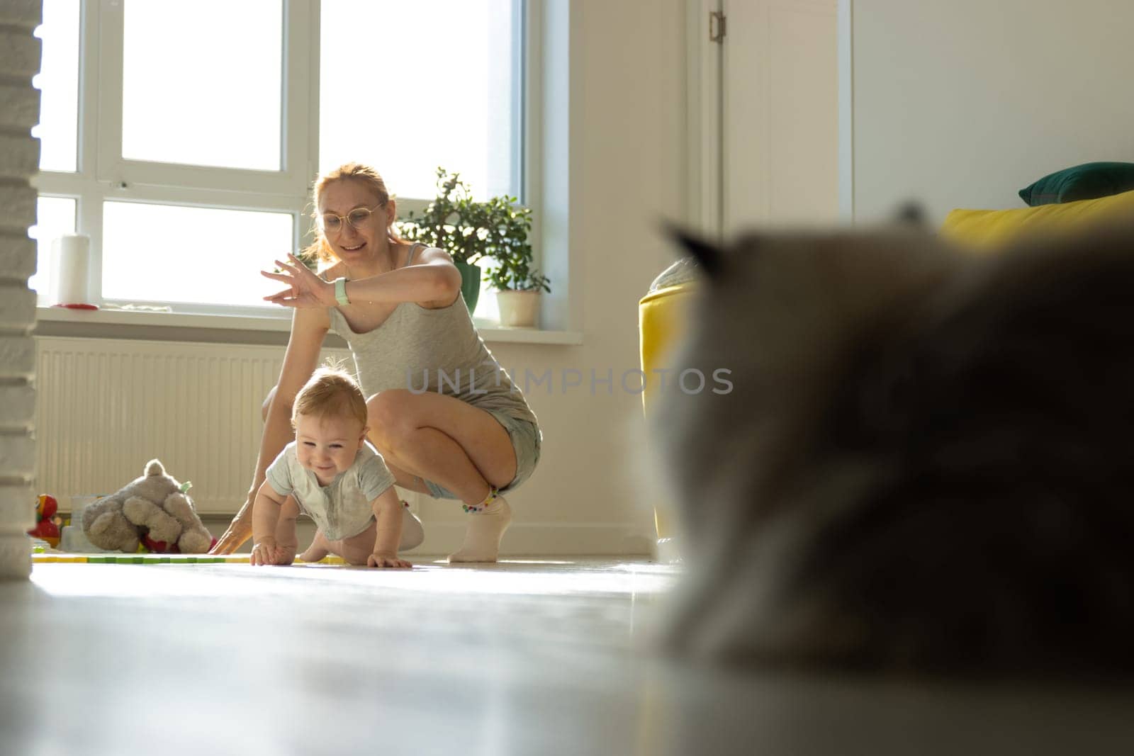 A woman kneeling down next to a baby and a cat