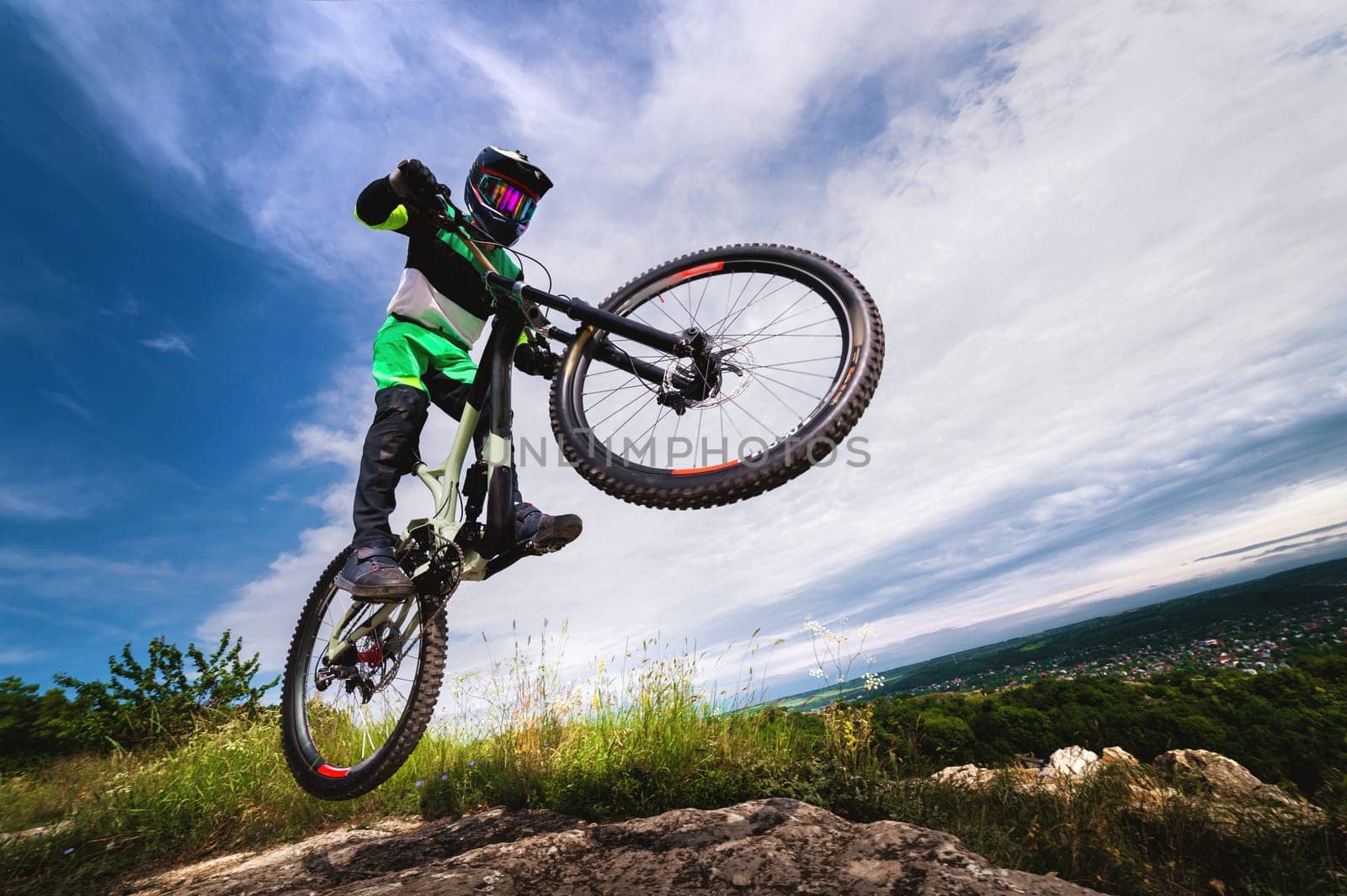 A professional racer jumps on a bicycle against a blue cloudy sky. Sunny summer day. Low angle view of a man on a mountain bike jumping in the mountains