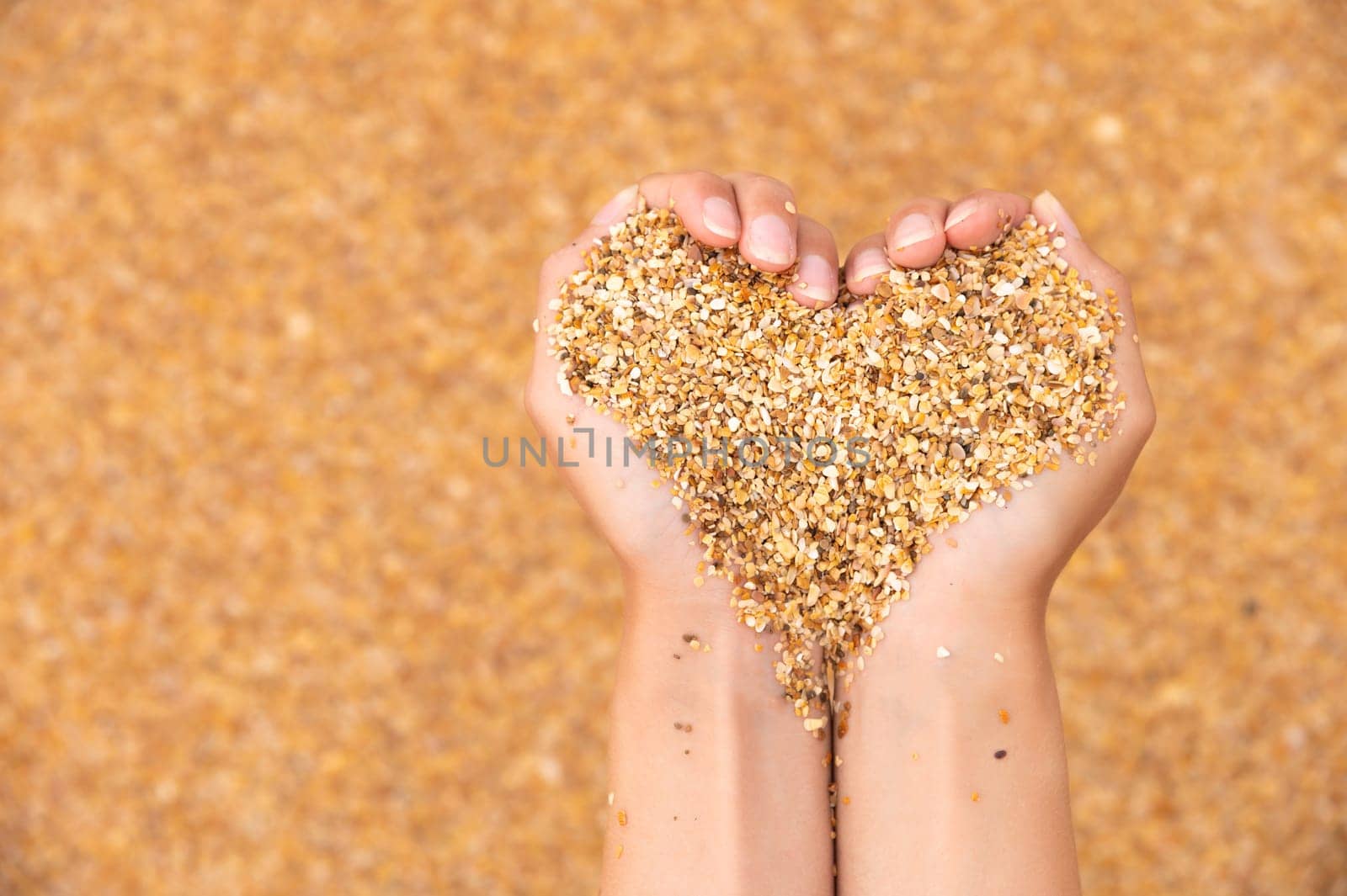 Hands hold sand in the shape of a heart. Close-up of woman's hands holding sand on the beach.