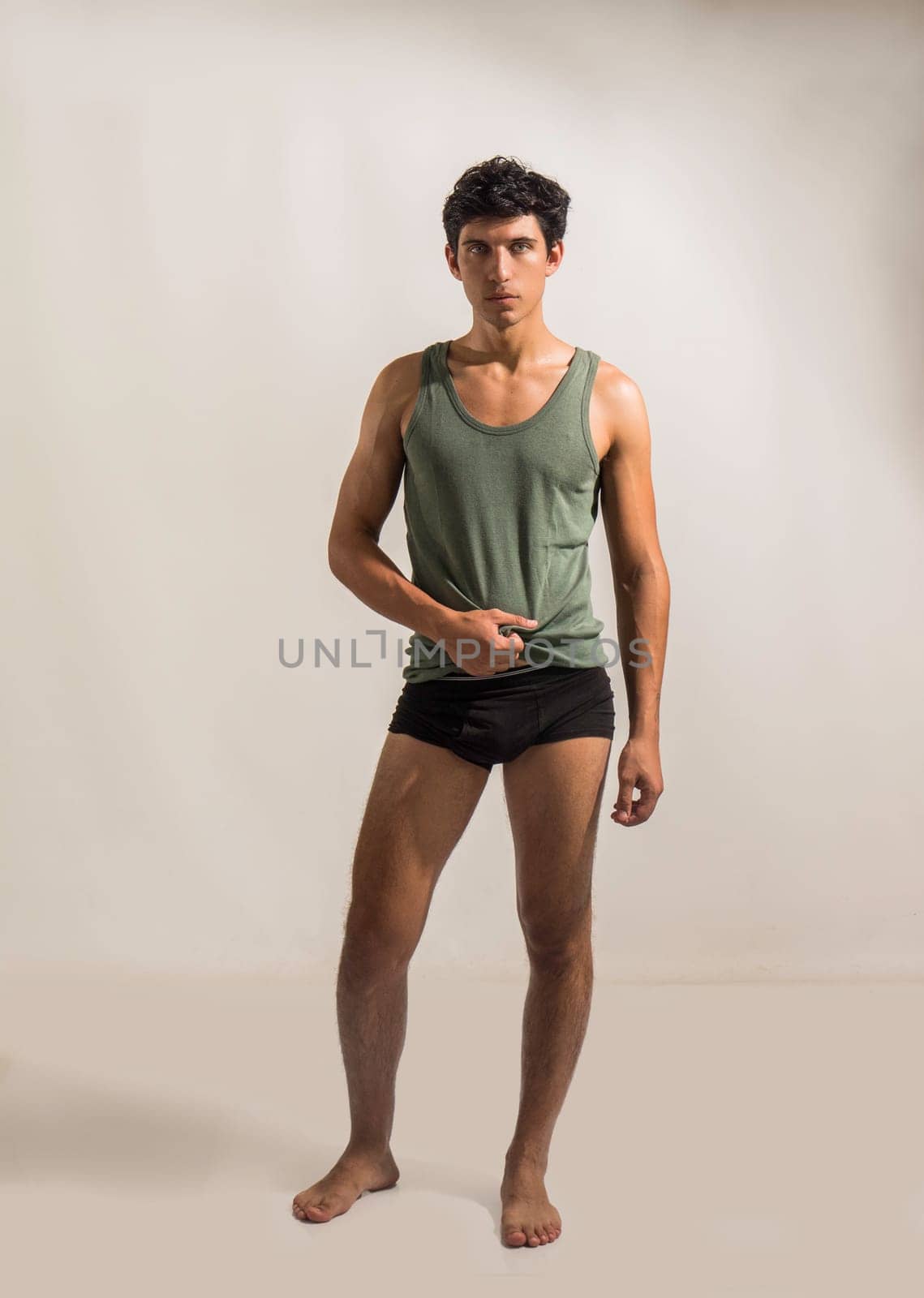 Full body view of fit and attractive young man in underwear on grey background. Wearing tank-top and looking at camera. Athletic fit physique