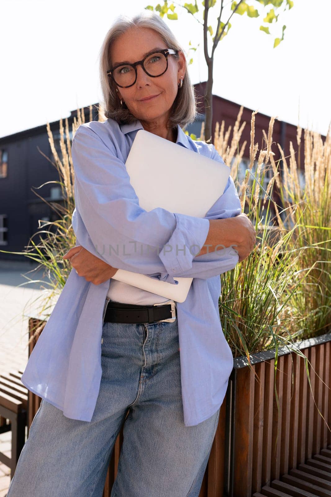 beautiful mature old woman with gray hair dressed checks mail on a laptop while walking down the street.