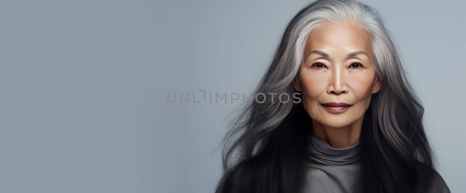 Smiling, elderly, gorgeous Asian woman gray long hair and perfect skin, on a gray background, banner. Advertising of cosmetic products, spa treatments, shampoos and hair care products, dentistry and medicine, perfumes and cosmetology for senior women