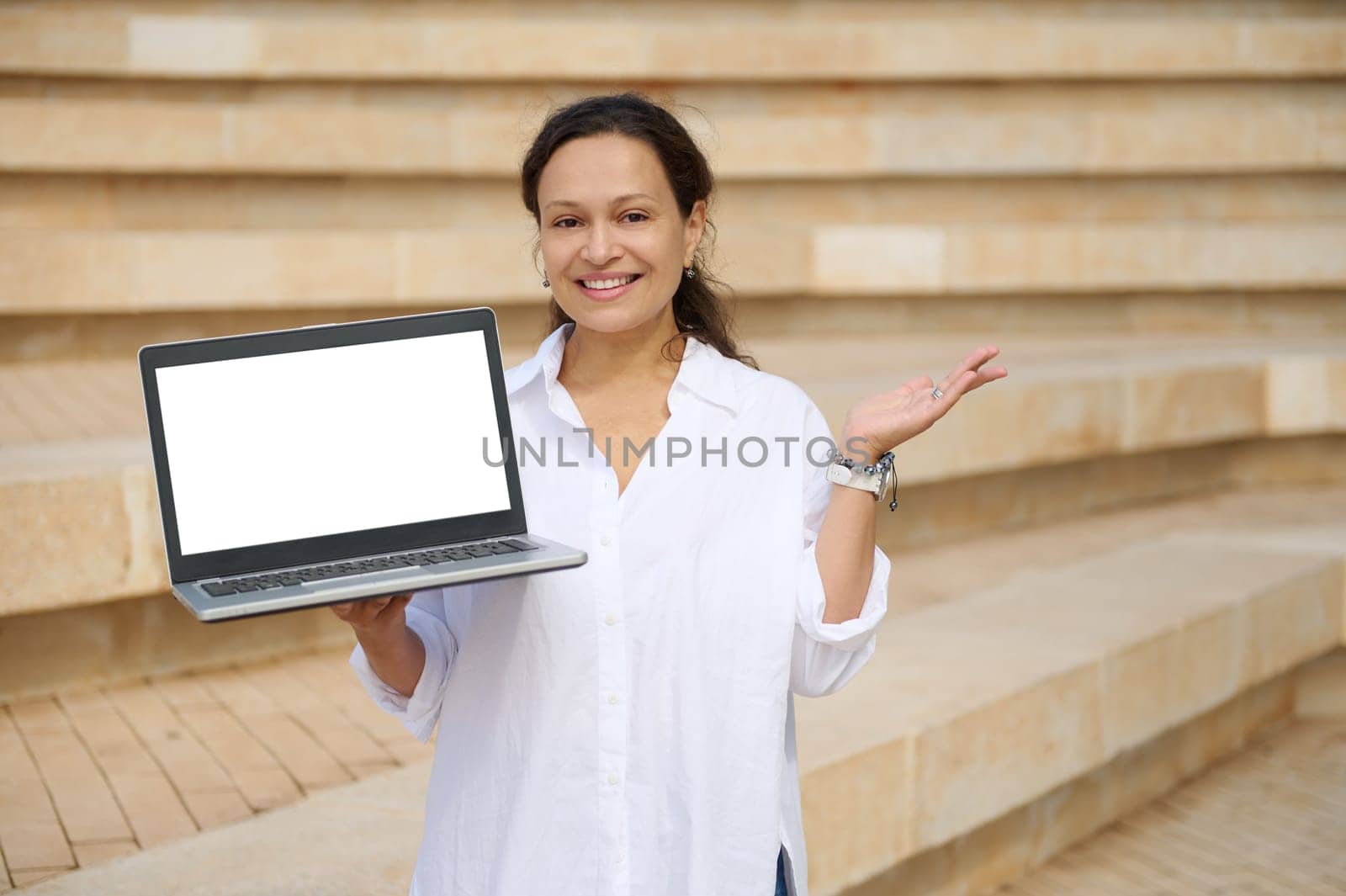 Confident female sales manager, trader, freelance entrepreneur broadly smiling looking at camera, holding laptop with white mockup digital screen. Copy advertising space