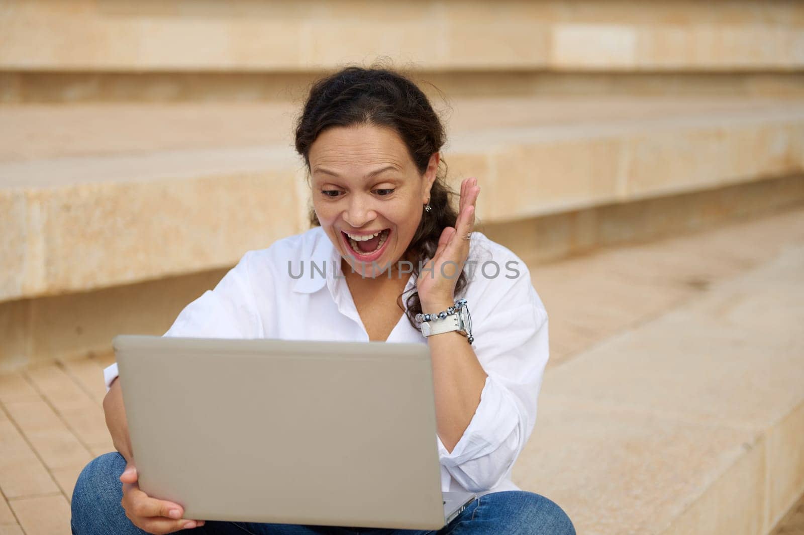 Happy latin young female student expressing positive emotions and clenching her fists while working on laptop, rejoicing at successfully passing university exams. People. Education. Online training