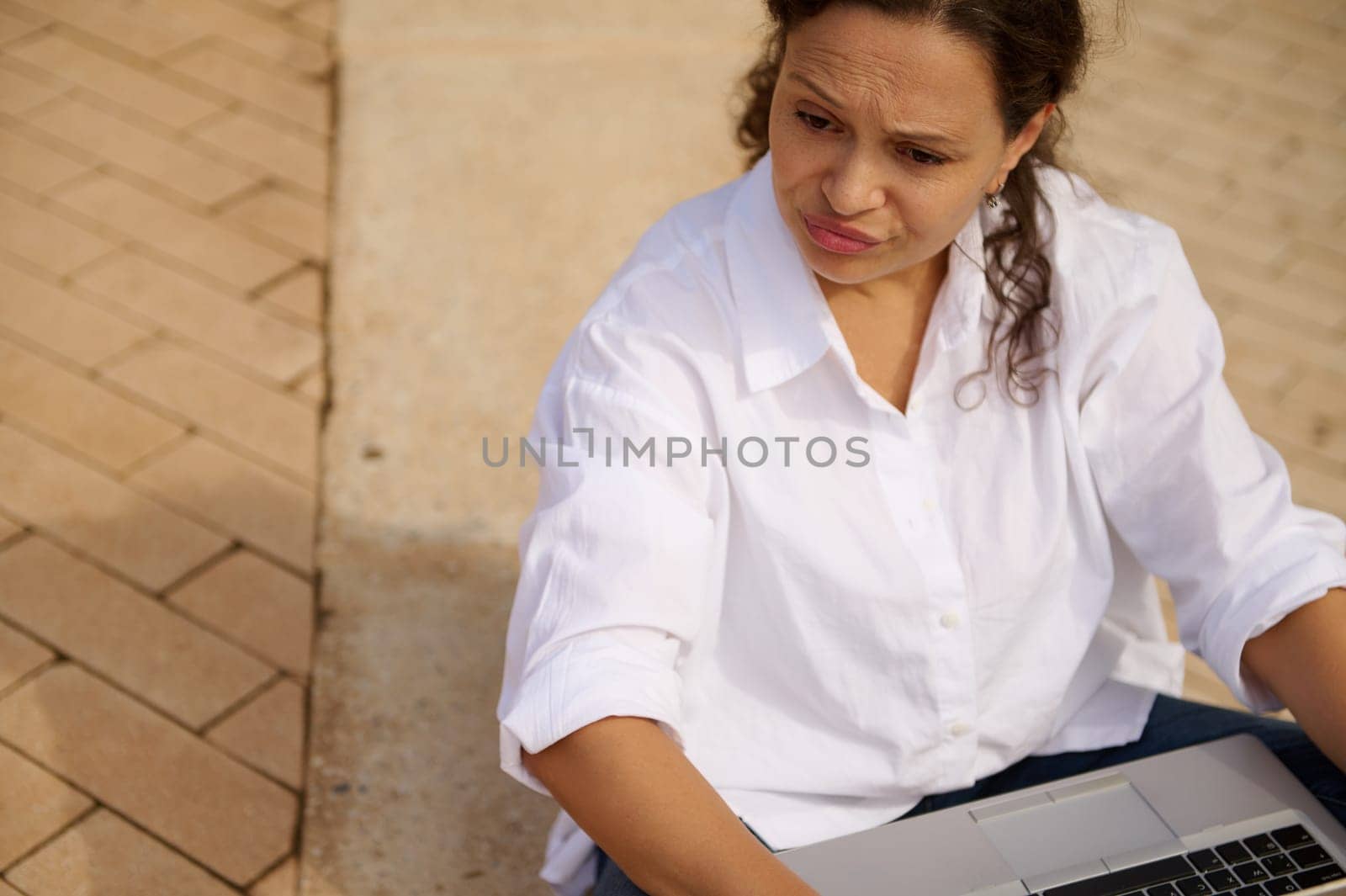 Close-up portrait of mixed race young adult woman expressing sadness failing business tender project, desperately and thoughtfully looking aside, sitting with laptop outdoors. Brainstorming Career Job