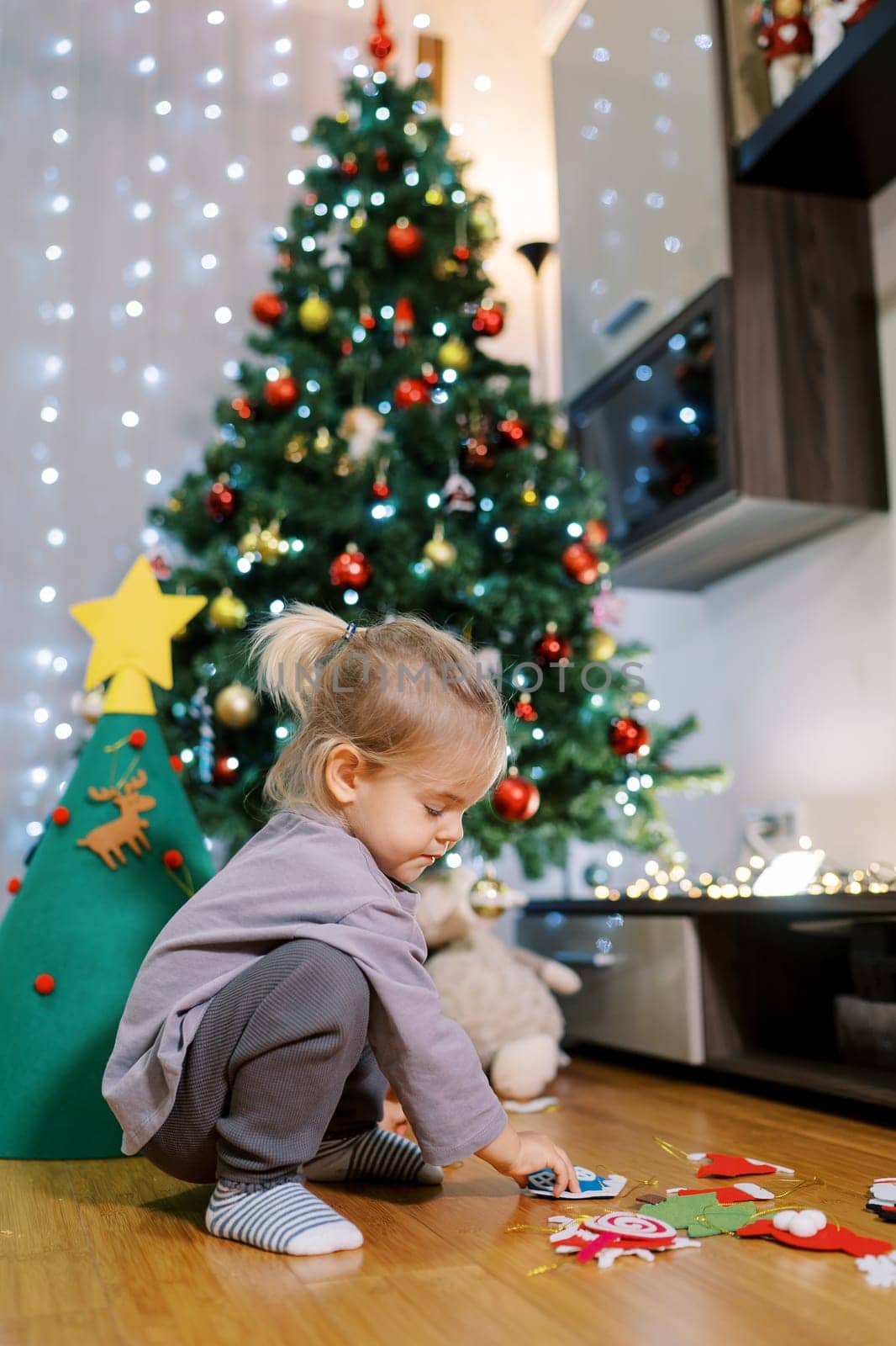 Little girl sorts out toys for a felt Christmas tree while squatting by Nadtochiy