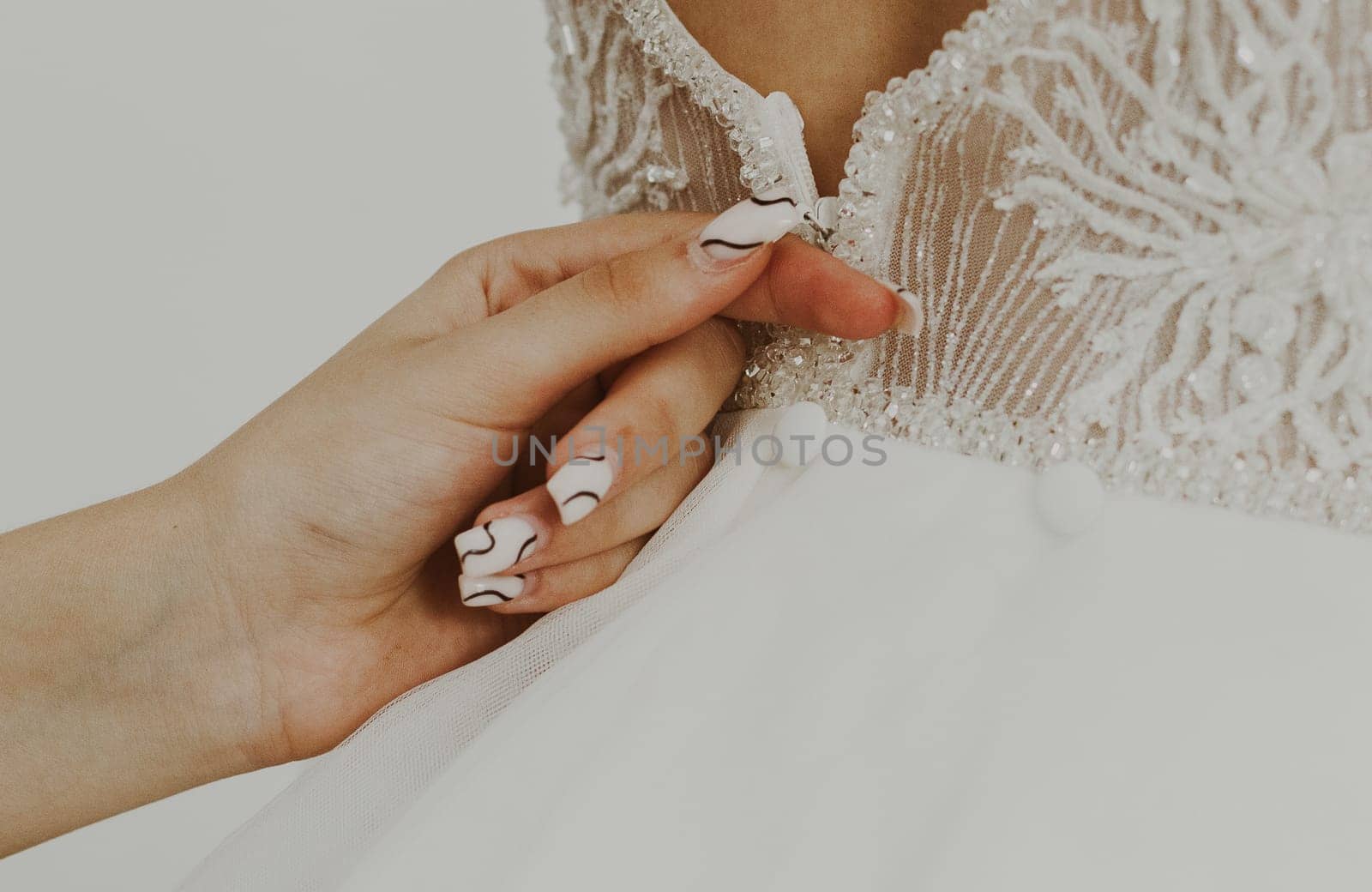 Young Caucasian girl zipping wedding dress on the back of the bride, close-up view from the side.