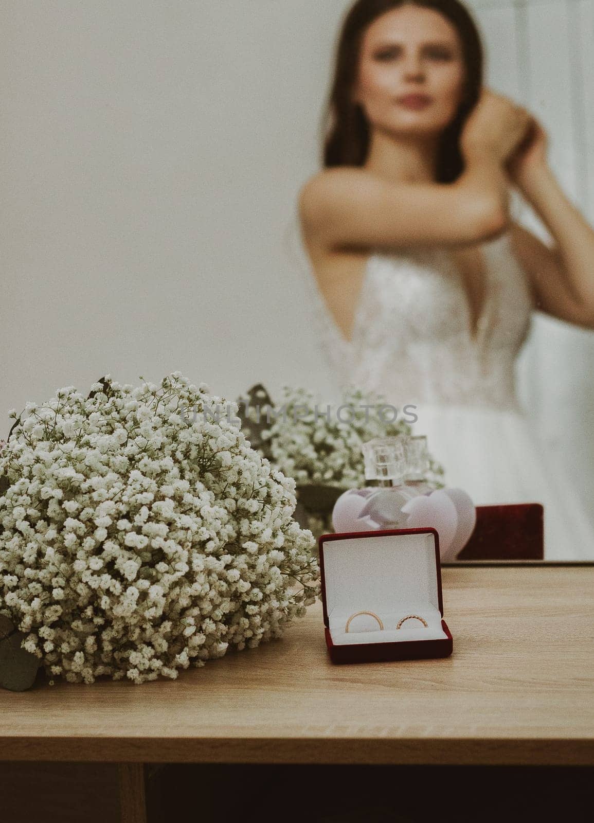 One wedding bouquet of boutonnieres and wedding rings in a box lying on a table with a blurred reflection of the bride in a mirror, side view close-up.