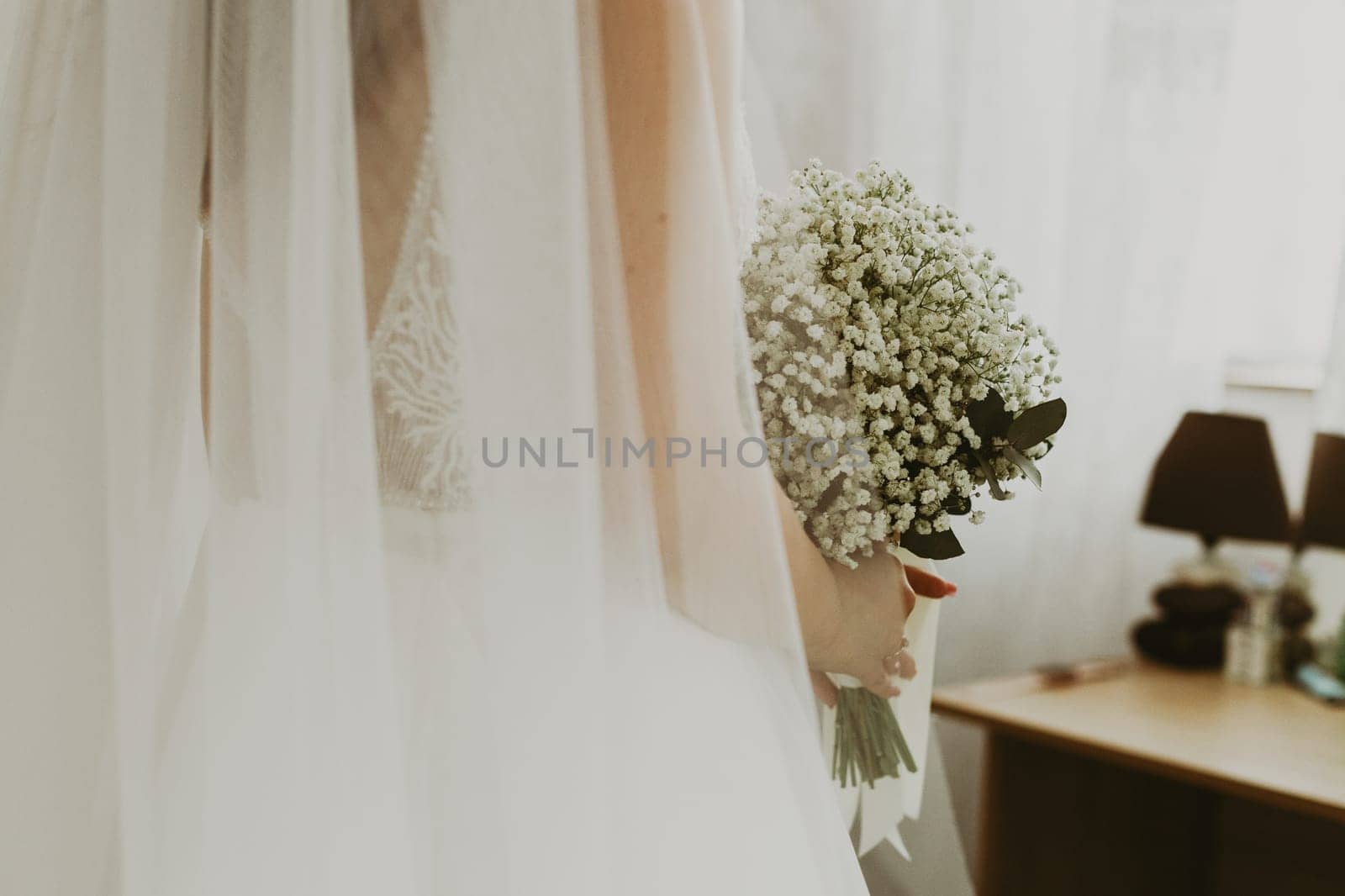 Portrait of one beautiful young Caucasian unrecognizable bride holding a bouquet of white boutonnieres in a room during the day, bottom view, close-up with selective focus.