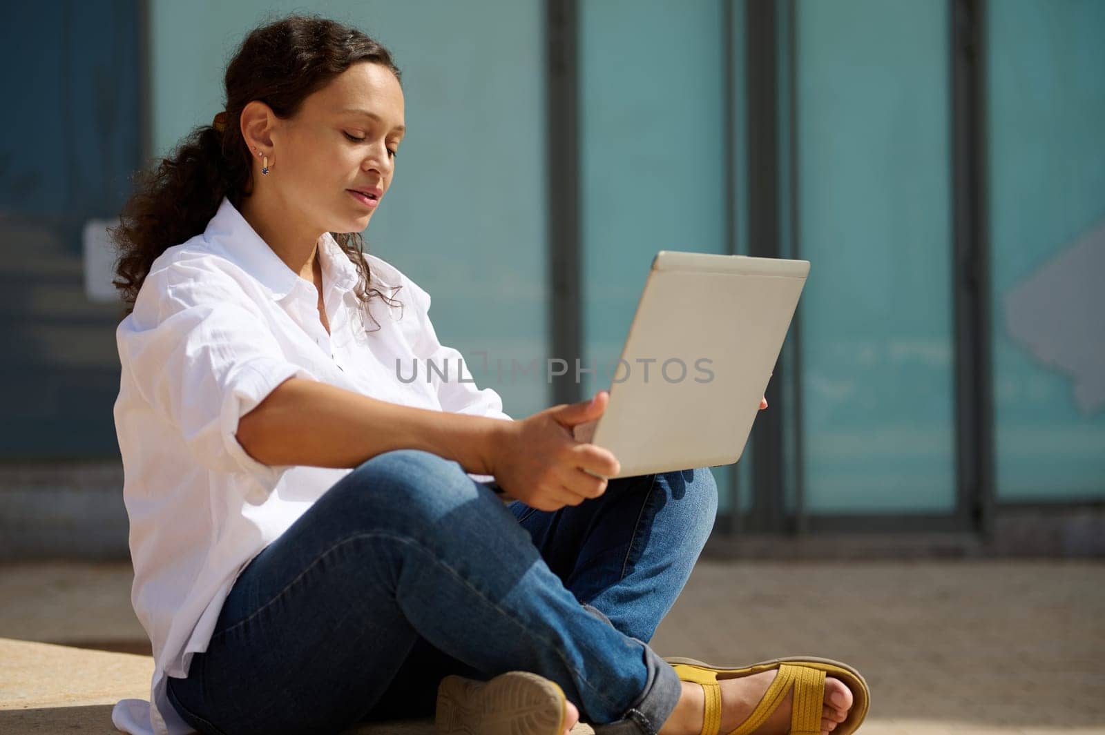 Confident young adult female student of university sitting on steps outdoors, doing online project for her diploma. People. Internet. Education. Knowledge. Career and recruitment concept. Copy space