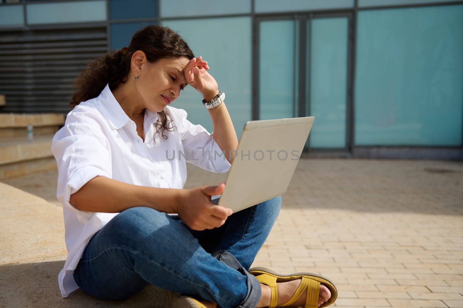 Multitasking businesswoman, manager, entrepreneur online working on laptop, thinking on strategy of business development and sales growth, sitting on steps outdoors. Brainstorming. People. Career