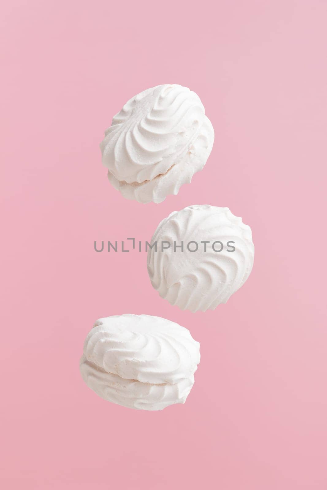 Soaring white zephyr marshmallow on pink background. flying food levitation, sweet candy dessert.