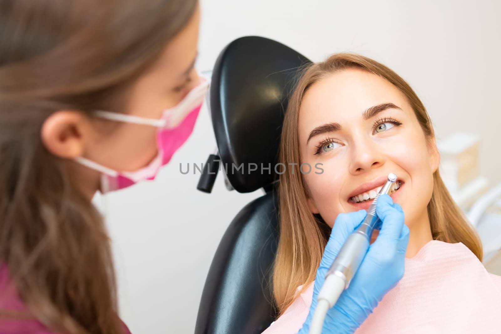 A dentist carefully doing a teeth grinding procedure to a graceful woman, improving the aesthetics of her smile