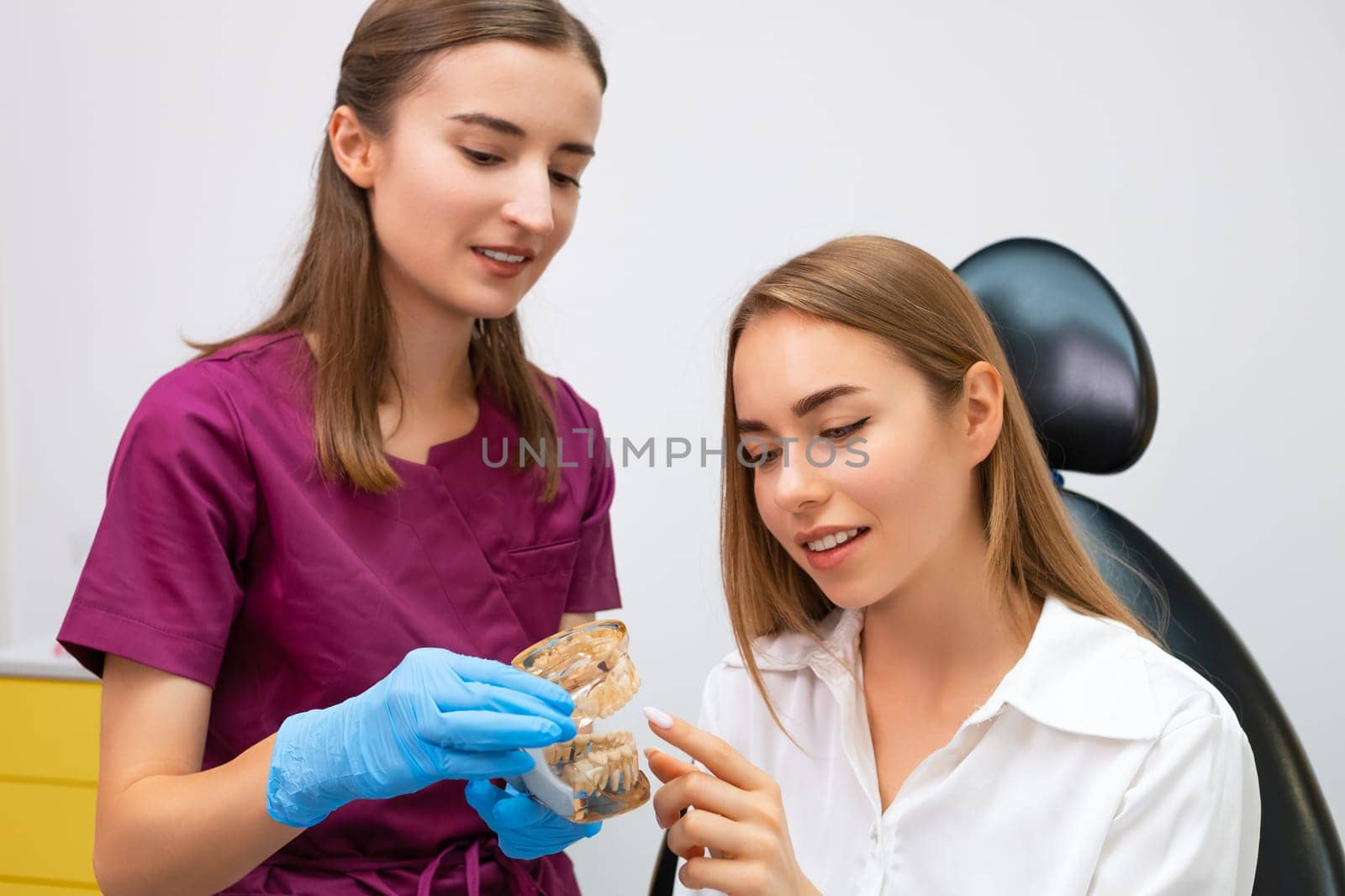 Orthodontist explains the procedure of alignment of teeth to the patient using a jaw layout in modern dentistry clinic